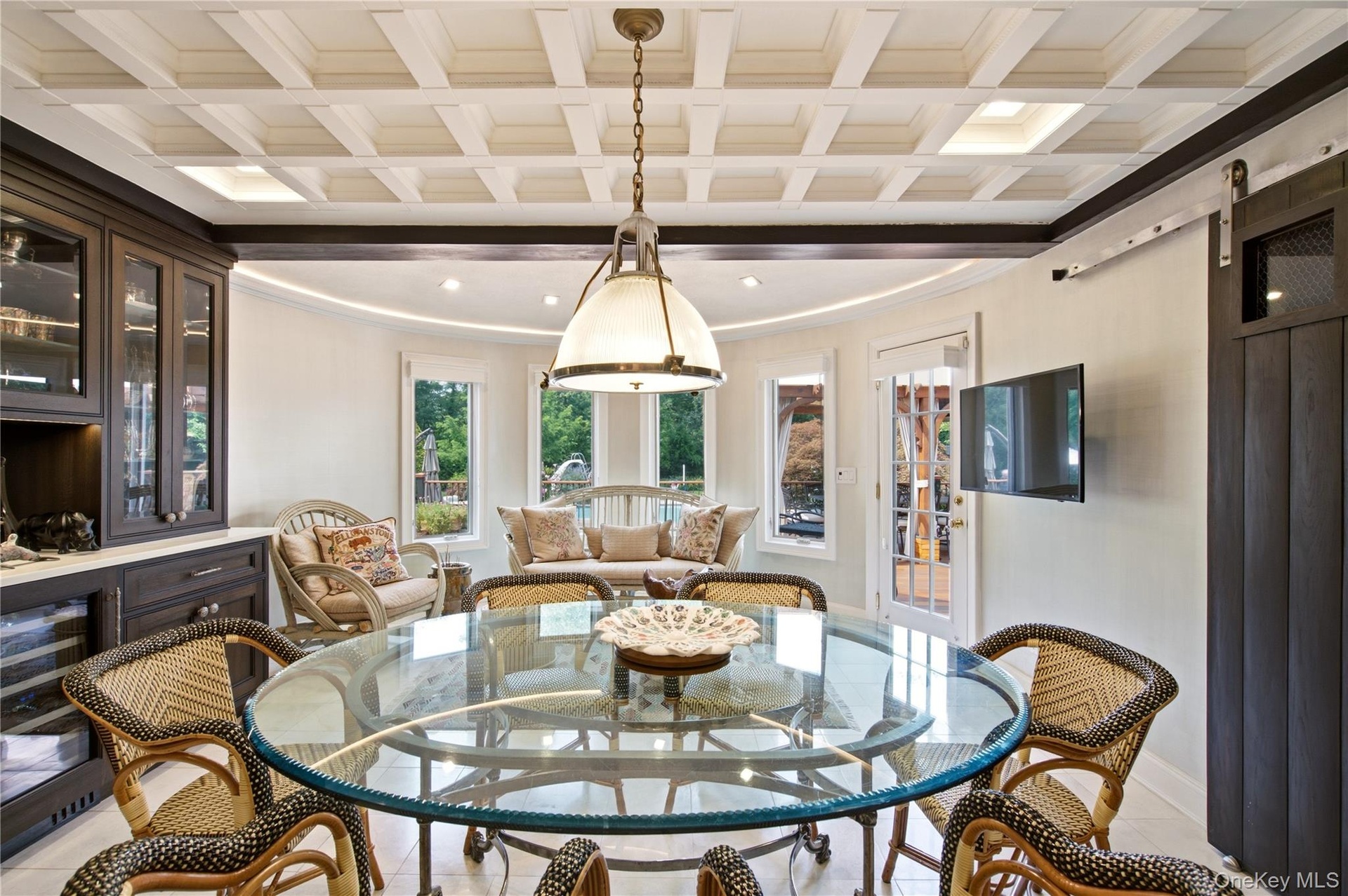 Recessed lighting illuminating a coffered ceiling, with glass-front cabinetry, a glass-top dining table, a white French door, and a dark wood-finish b
