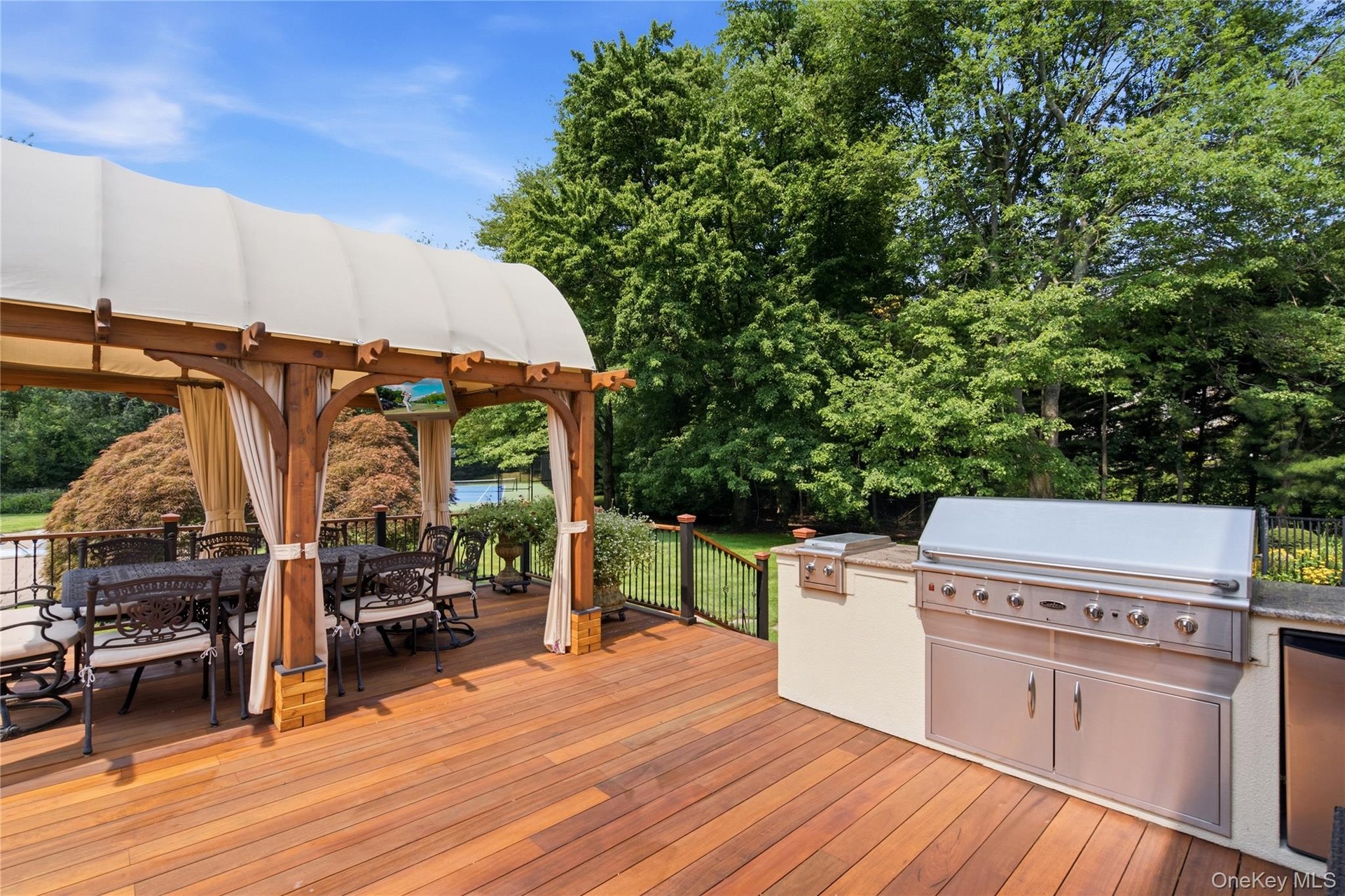 Expansive wood-finish deck featuring a covered pergola, built-in outdoor kitchen with stainless steel appliances.