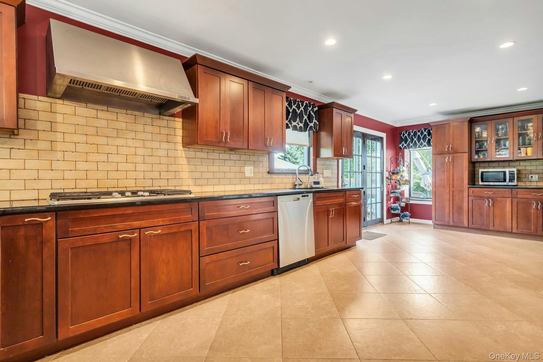 Kitchen featuring wood cabinetry, stainless steel range hood, tile backsplash, black countertops, and recessed lighting