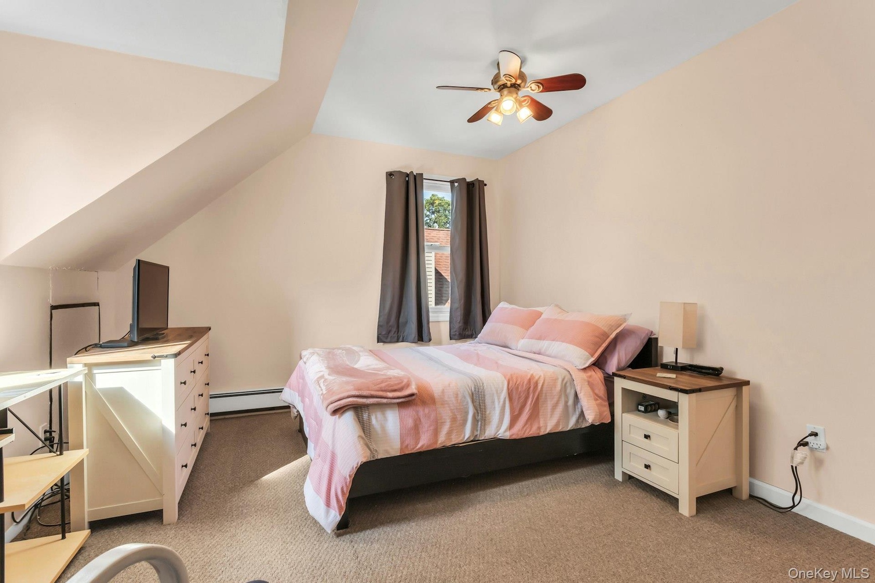 Sloped ceiling room featuring a ceiling fan, carpeted flooring, and a single window with curtains