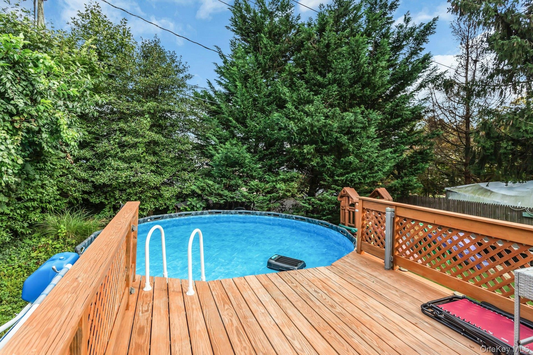 Wood-finish decking surrounding an above-ground swimming pool with integrated entry steps and a lattice-style wood railing