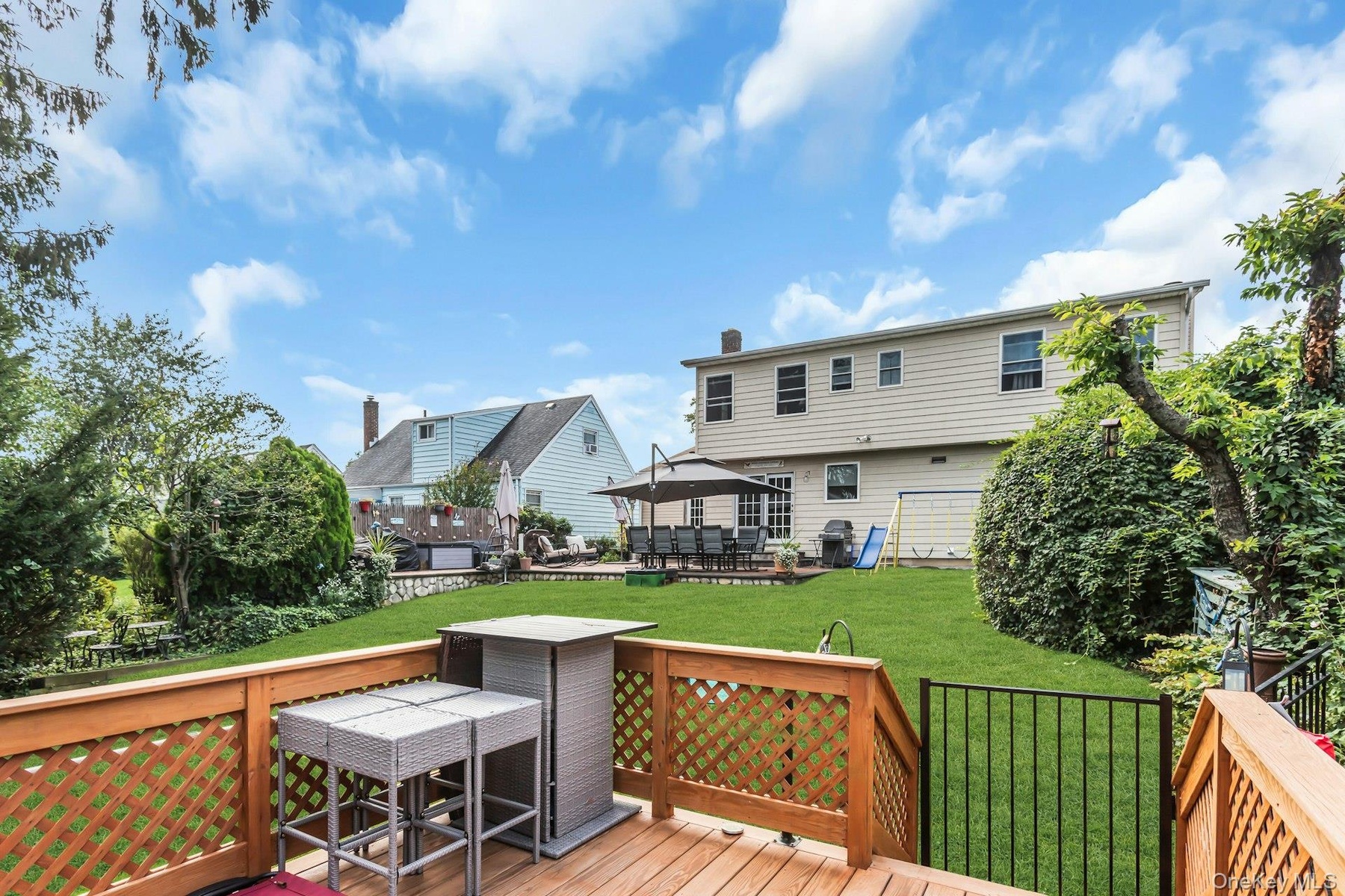 Wood-finish deck with lattice railing, private green lawn, mature perimeter landscaping, and a back patio