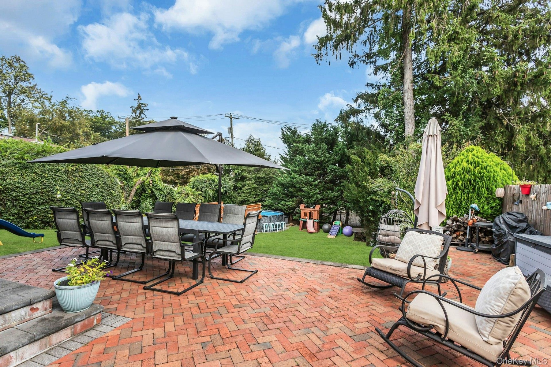 Expansive backyard featuring a red brick patio, a manicured lawn, and mature perimeter trees