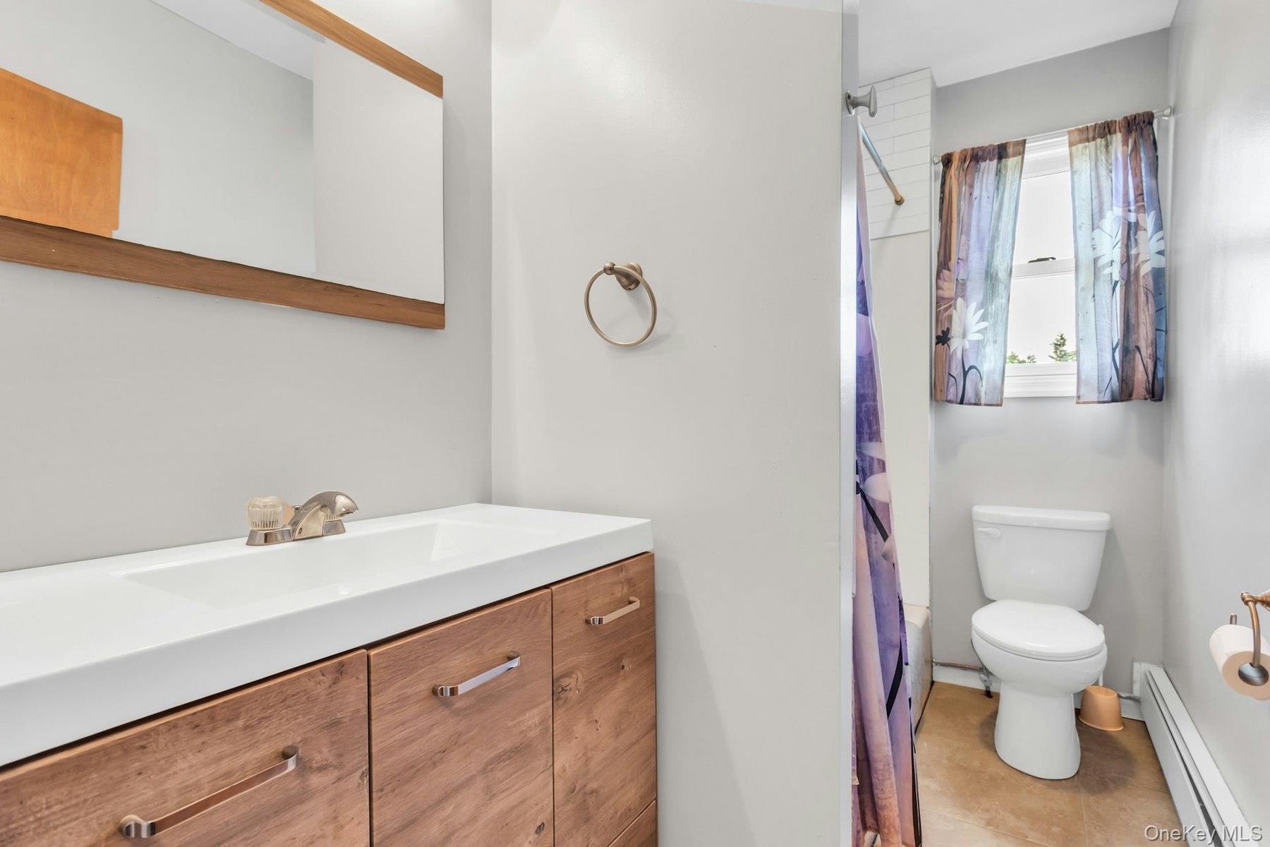 Bathroom featuring a wood-finish vanity with an integrated sink, a framed mirror, and a window with a white frame