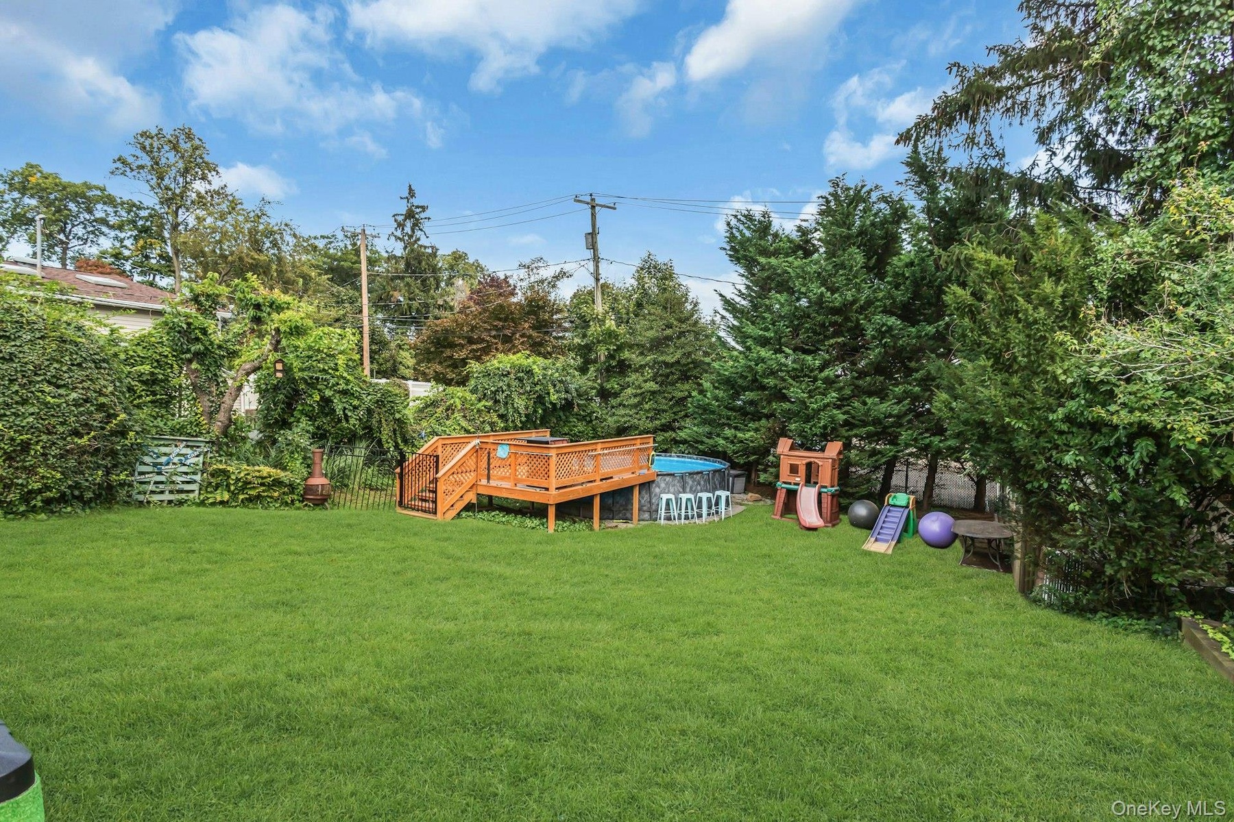 Expansive green lawn featuring a wooden deck, an above-ground pool, and mature perimeter trees