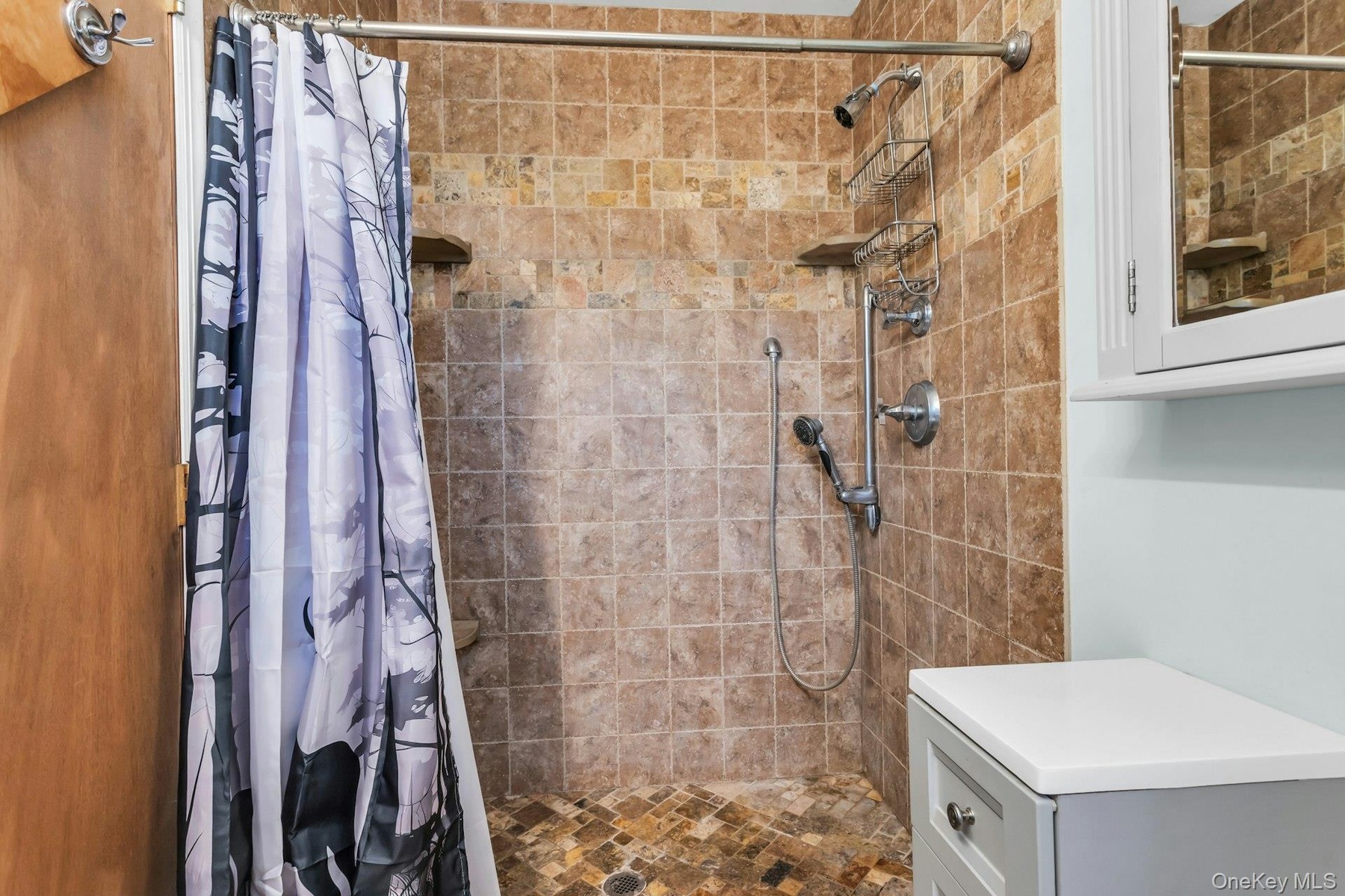 Tiled shower enclosure featuring a handheld showerhead and built-in shelving