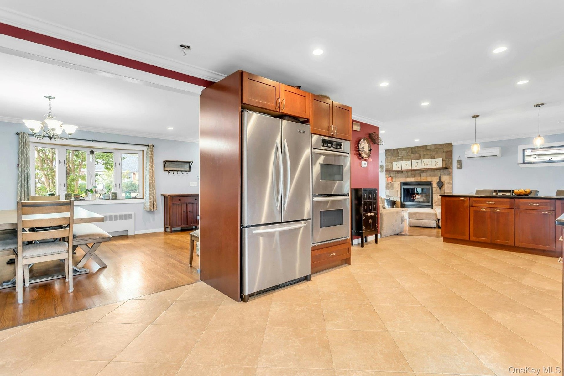 Stainless steel double oven, integrated stainless steel refrigerator, kitchen island with dark countertop, stone-clad fireplace, and recessed lighting