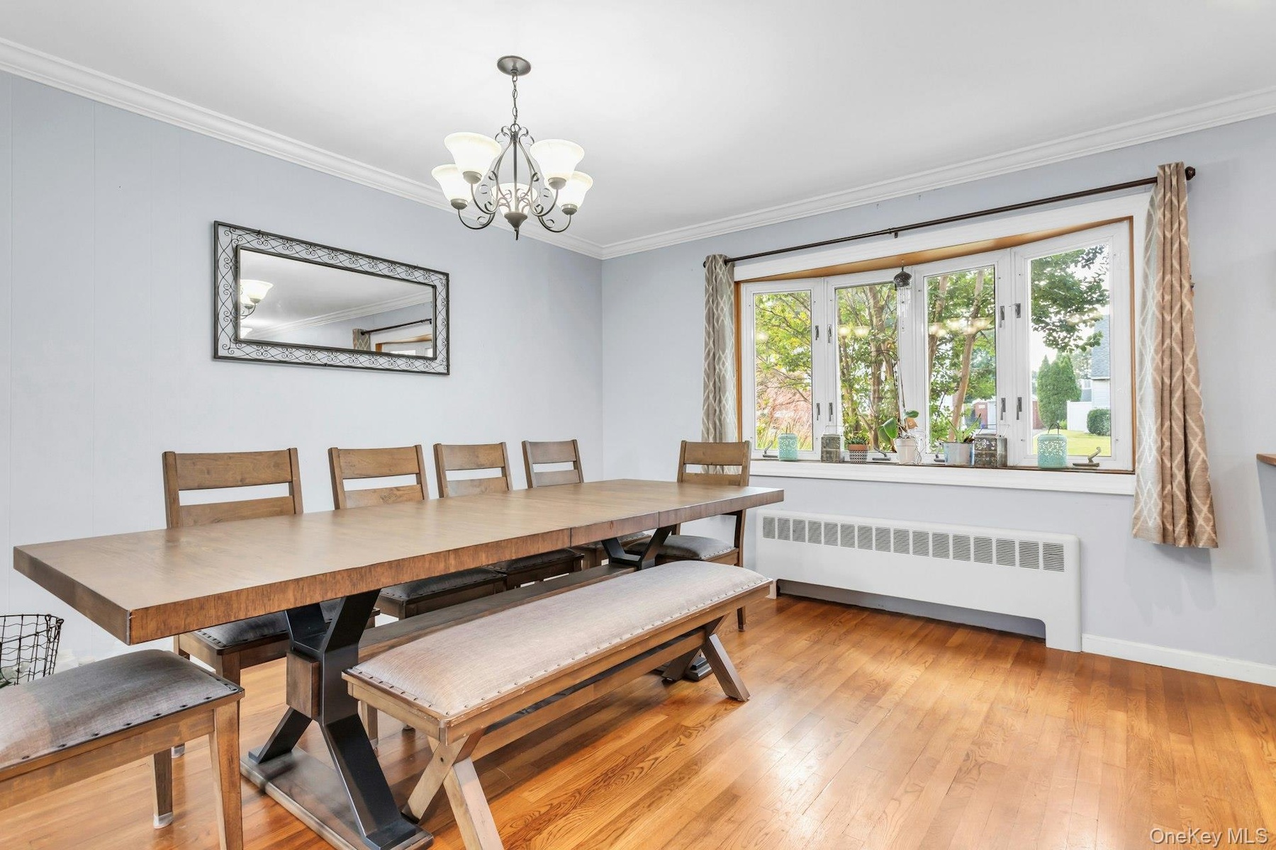 Hardwood flooring throughout, featuring a bay window with a wide sill, crown molding, and an overhead chandelier