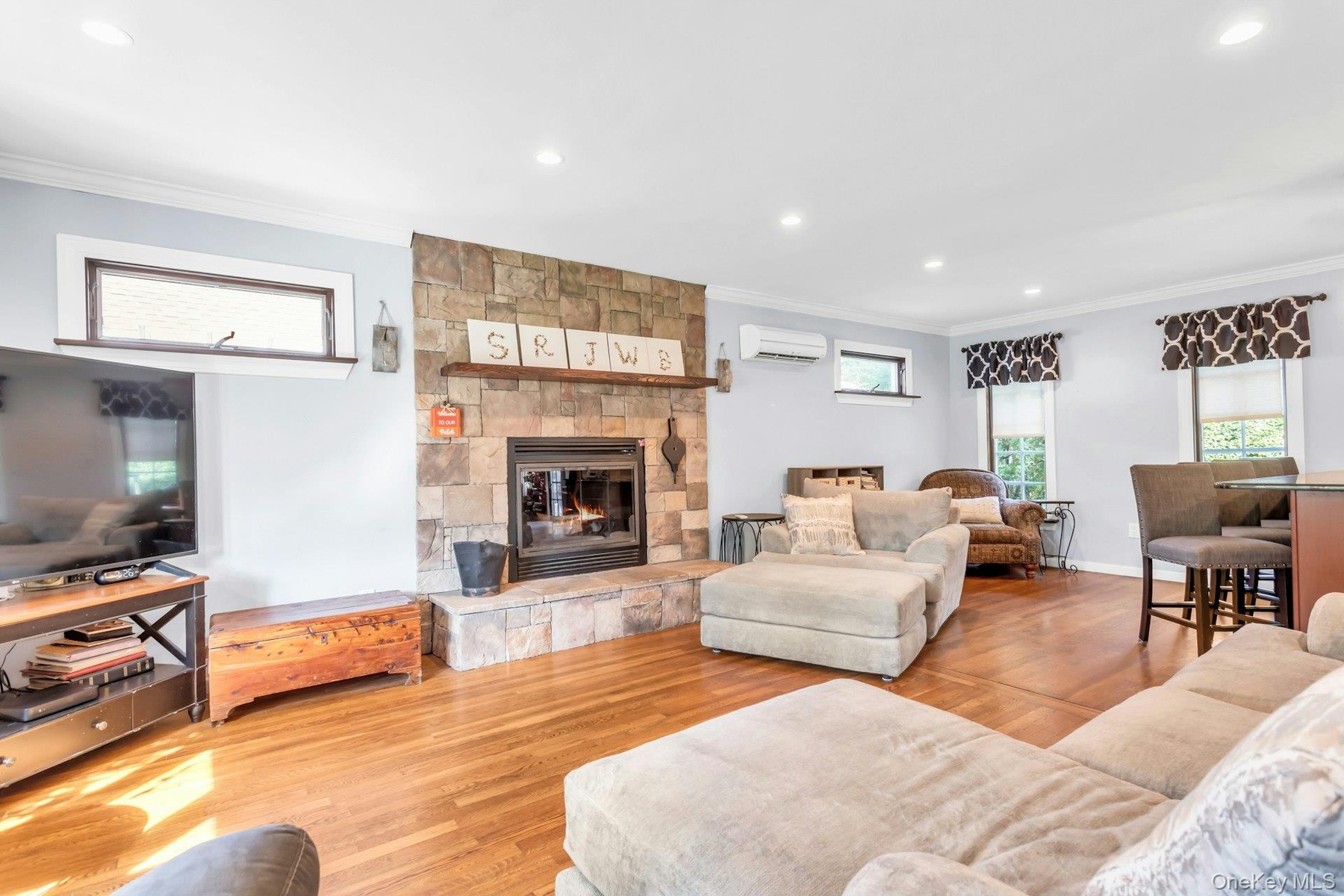 Stone-surround fireplace with hearth, wood-finish flooring, recessed lighting, crown molding, and clerestory windows