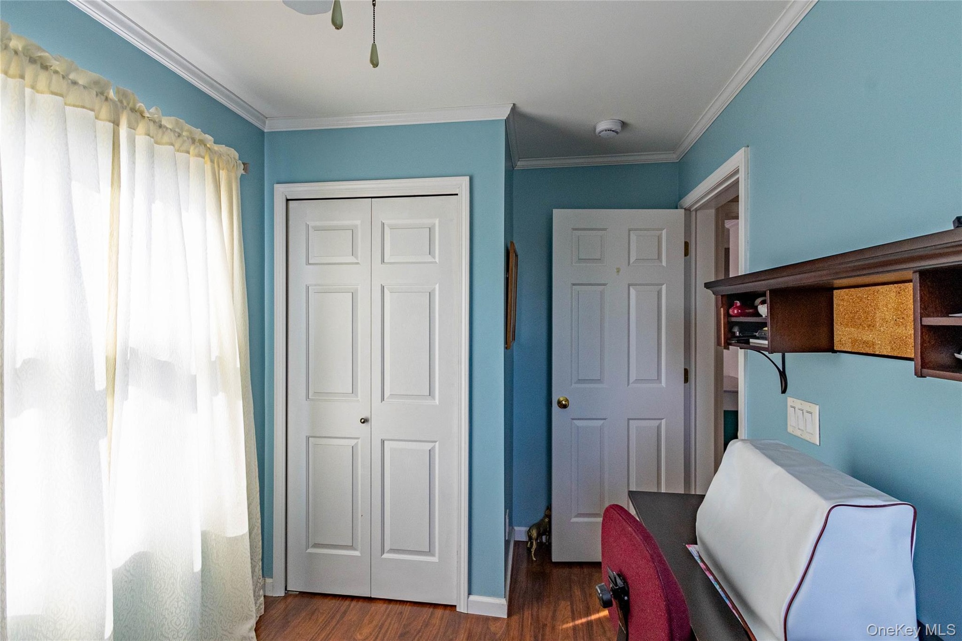 Wood-finish flooring, white bi-fold closet doors, white paneled interior door, crown molding, and built-in shelving unit