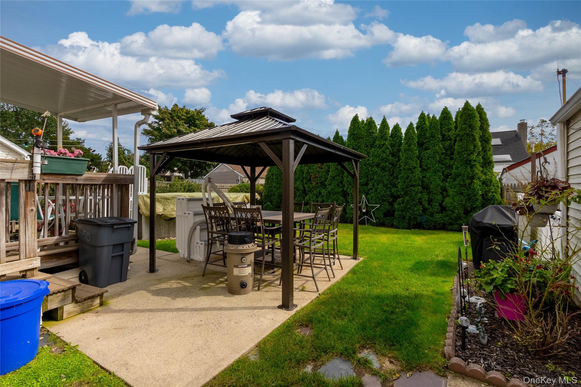 Expansive backyard featuring a concrete patio, freestanding gazebo, manicured lawn, and mature privacy trees