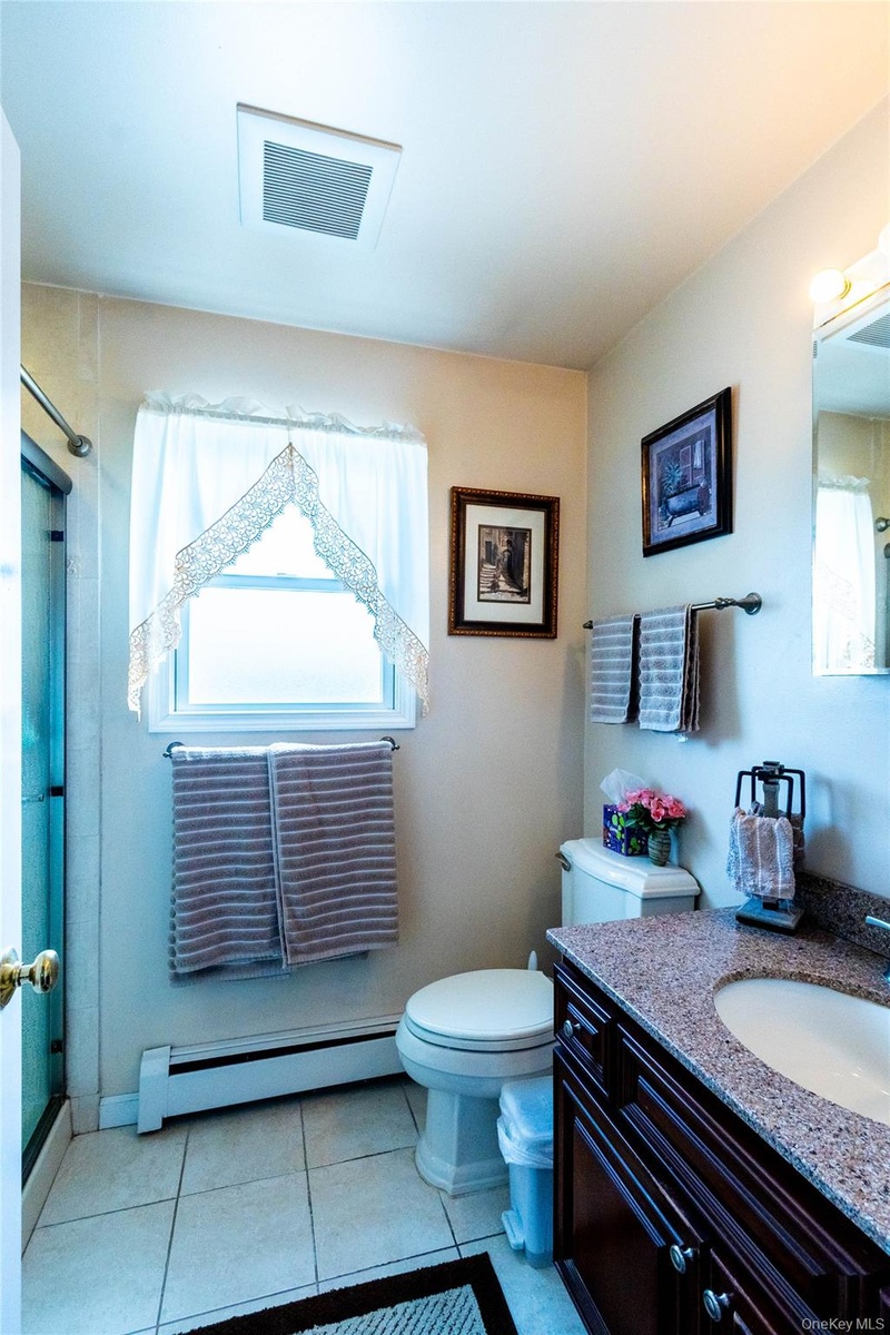 Bathroom featuring a dark wood-finish vanity with an integrated sink and granite-finish countertop, tiled flooring, and a window with natural light