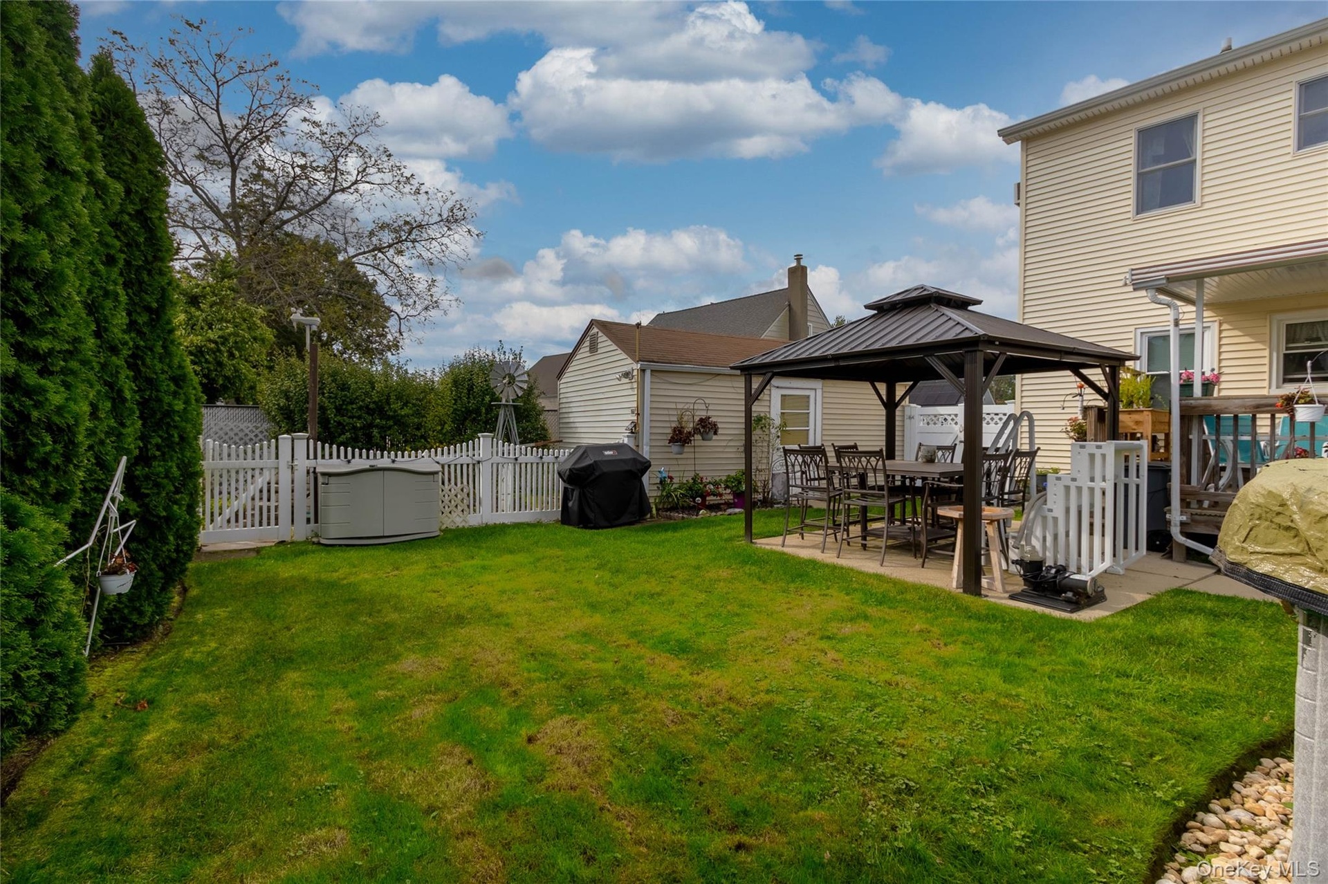 Expansive green lawn with a privacy hedge, white picket fencing, and a paved patio area
