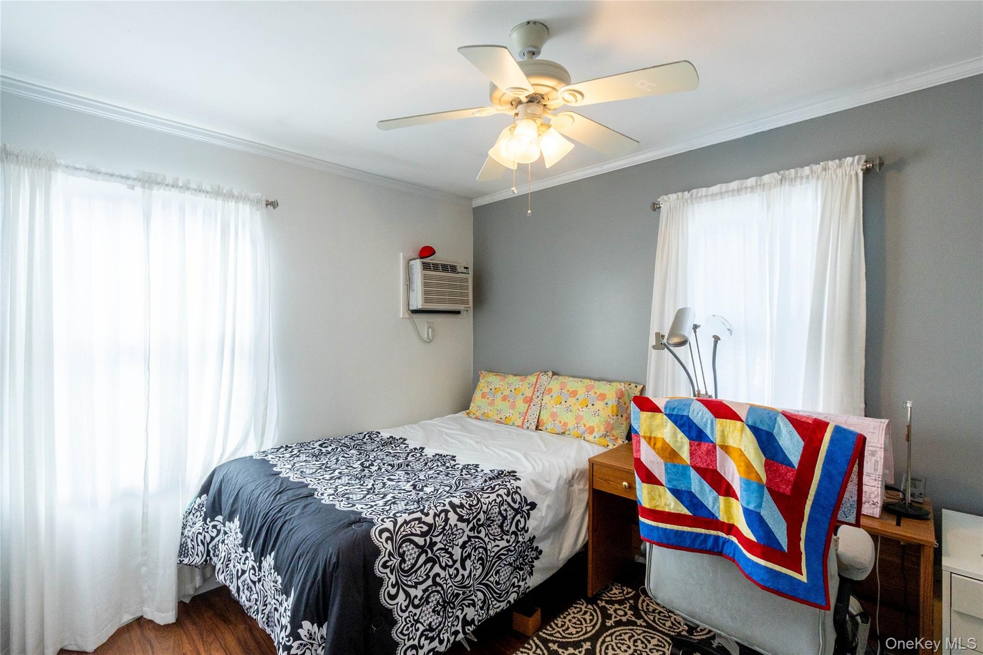 Wood-finish flooring, two windows, crown molding, and a ceiling fan with light fixture
