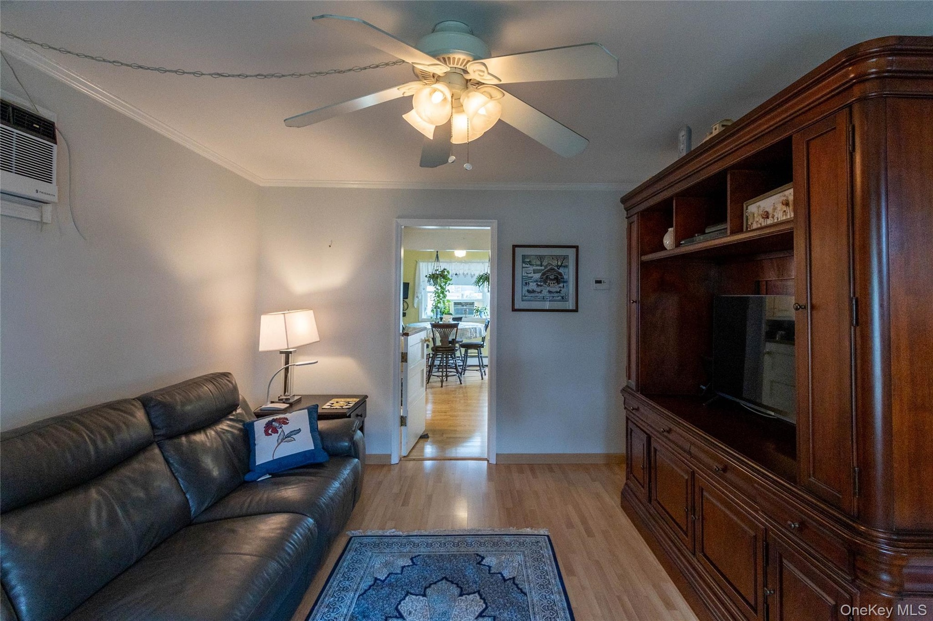 Wood-finish flooring throughout, ceiling fan with integrated lighting, and a built-in wood entertainment center with display shelving