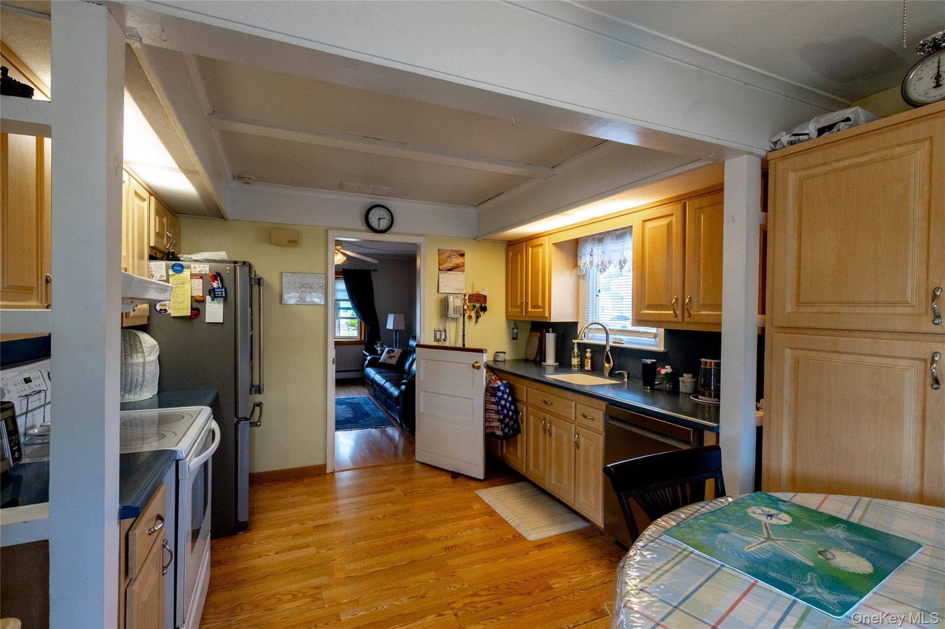 Wood-finish flooring, exposed ceiling beams, light wood-finish cabinetry, black countertops, and a stainless steel sink