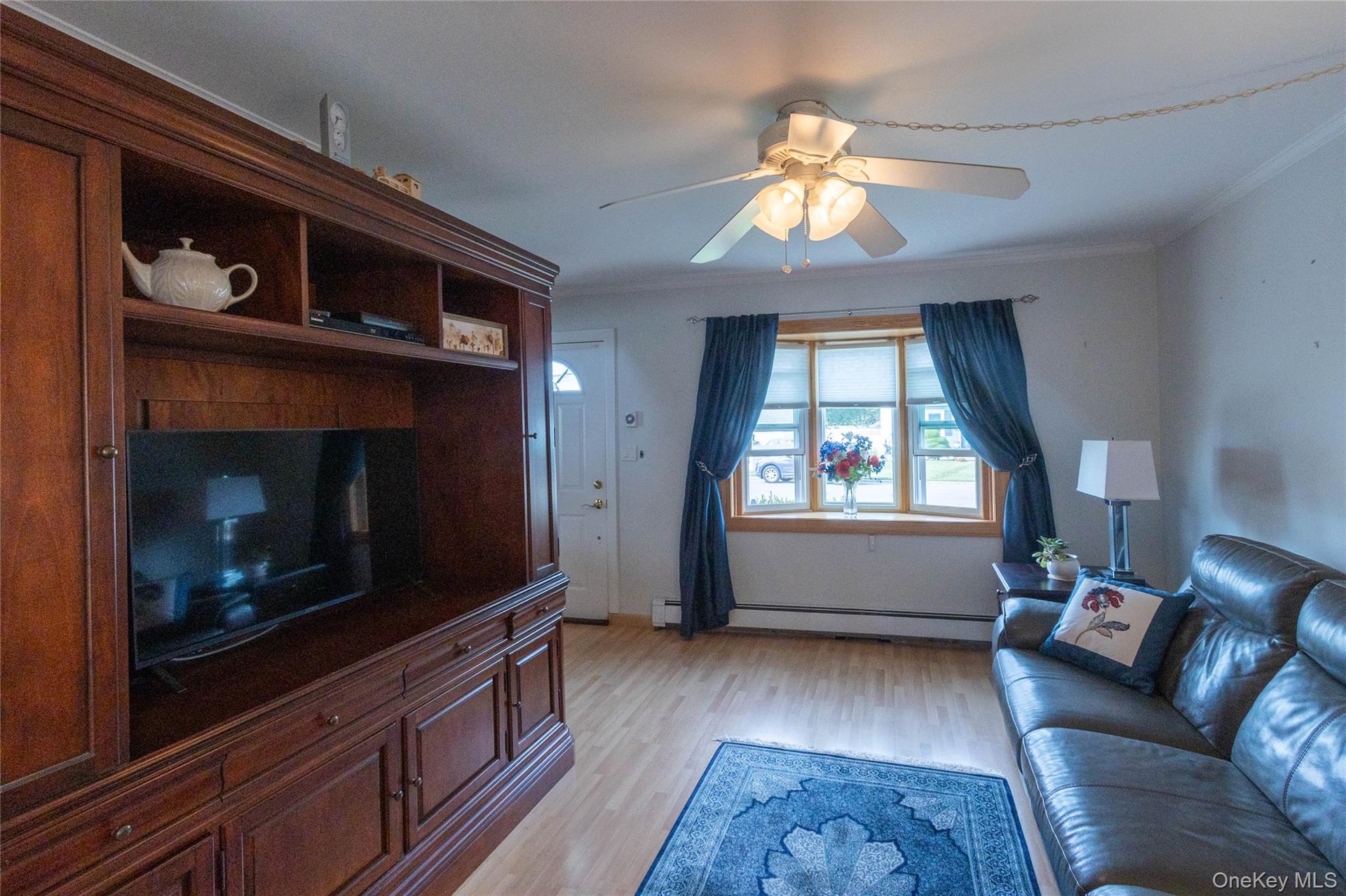 Wood-finish flooring, built-in entertainment center, bay window, ceiling fan, and crown molding