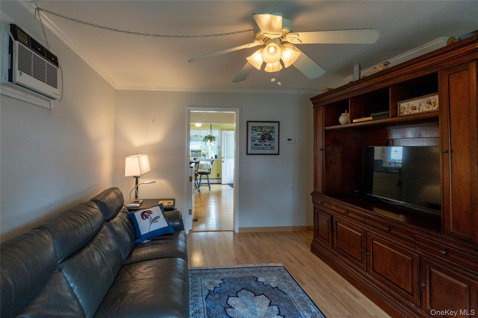 Hardwood-style flooring with a dark wood built-in media cabinet, crown molding, and a ceiling fan with integrated lighting