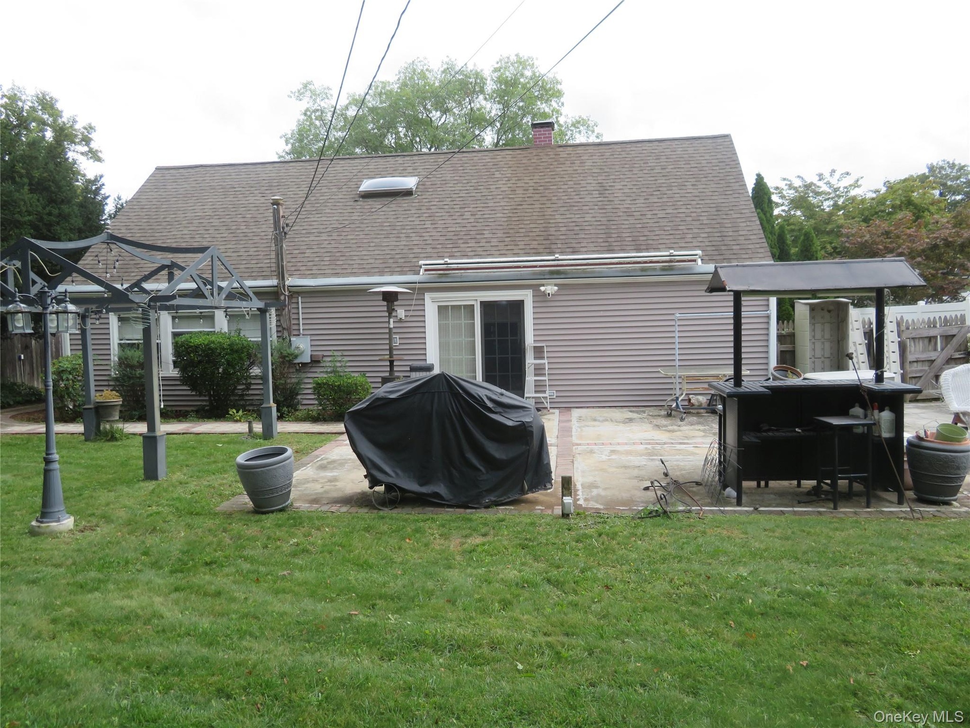 Expansive backyard with a concrete patio featuring a sliding glass door, a metal gazebo structure, and a secondary structure with a dark roof