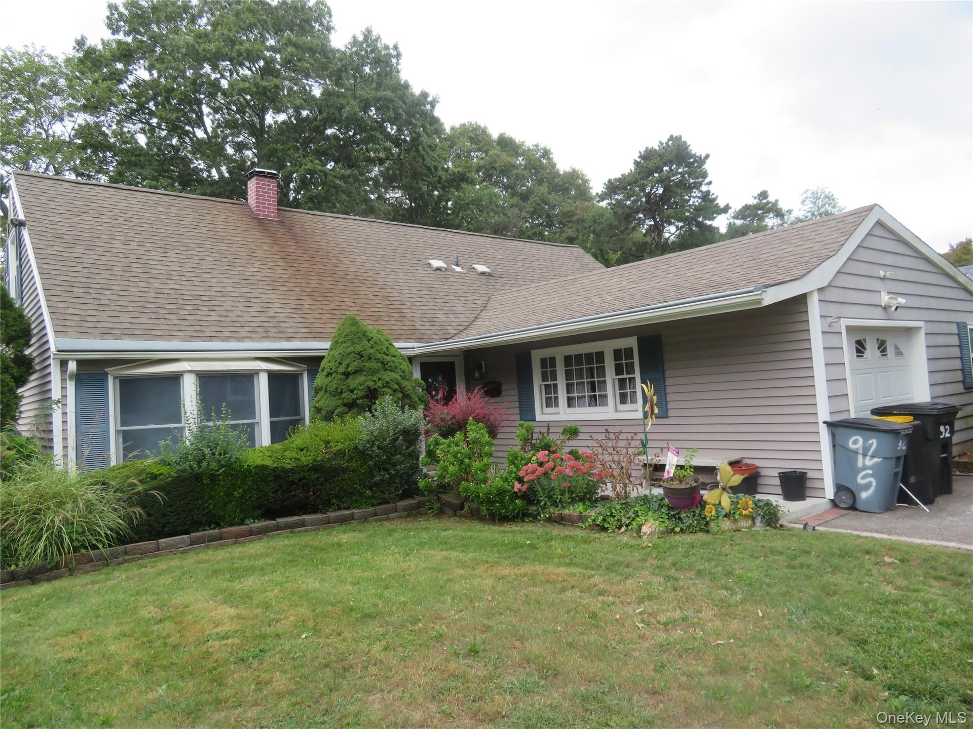 Front elevation featuring a brick chimney, bay window, attached garage, and manicured landscaping