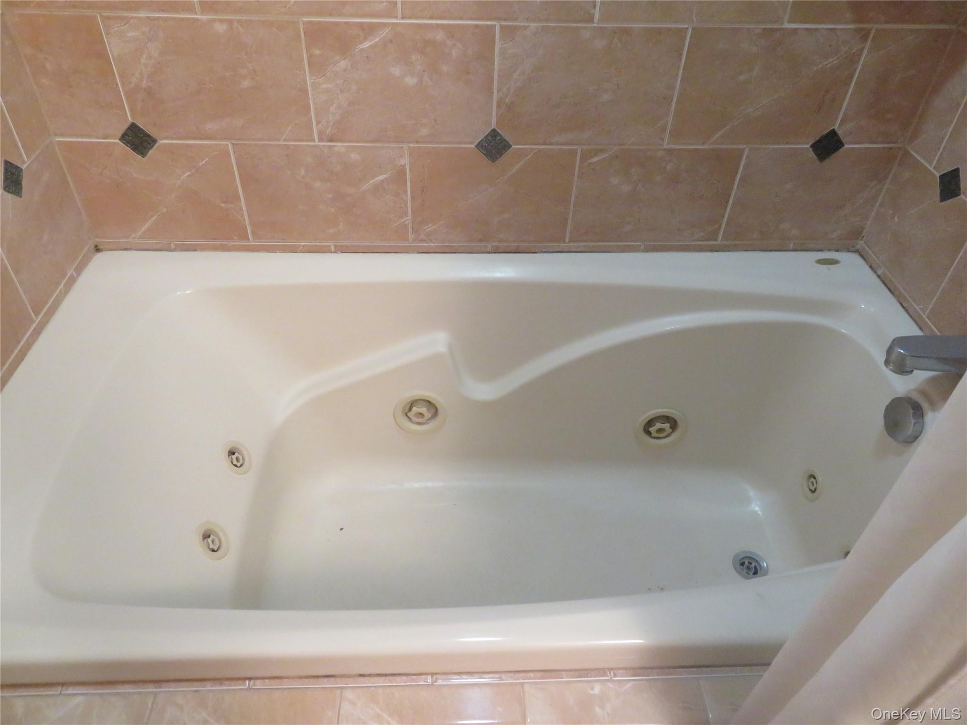 Built-in soaking tub with multiple jets, integrated bath faucet, and surrounding tile work with decorative accents