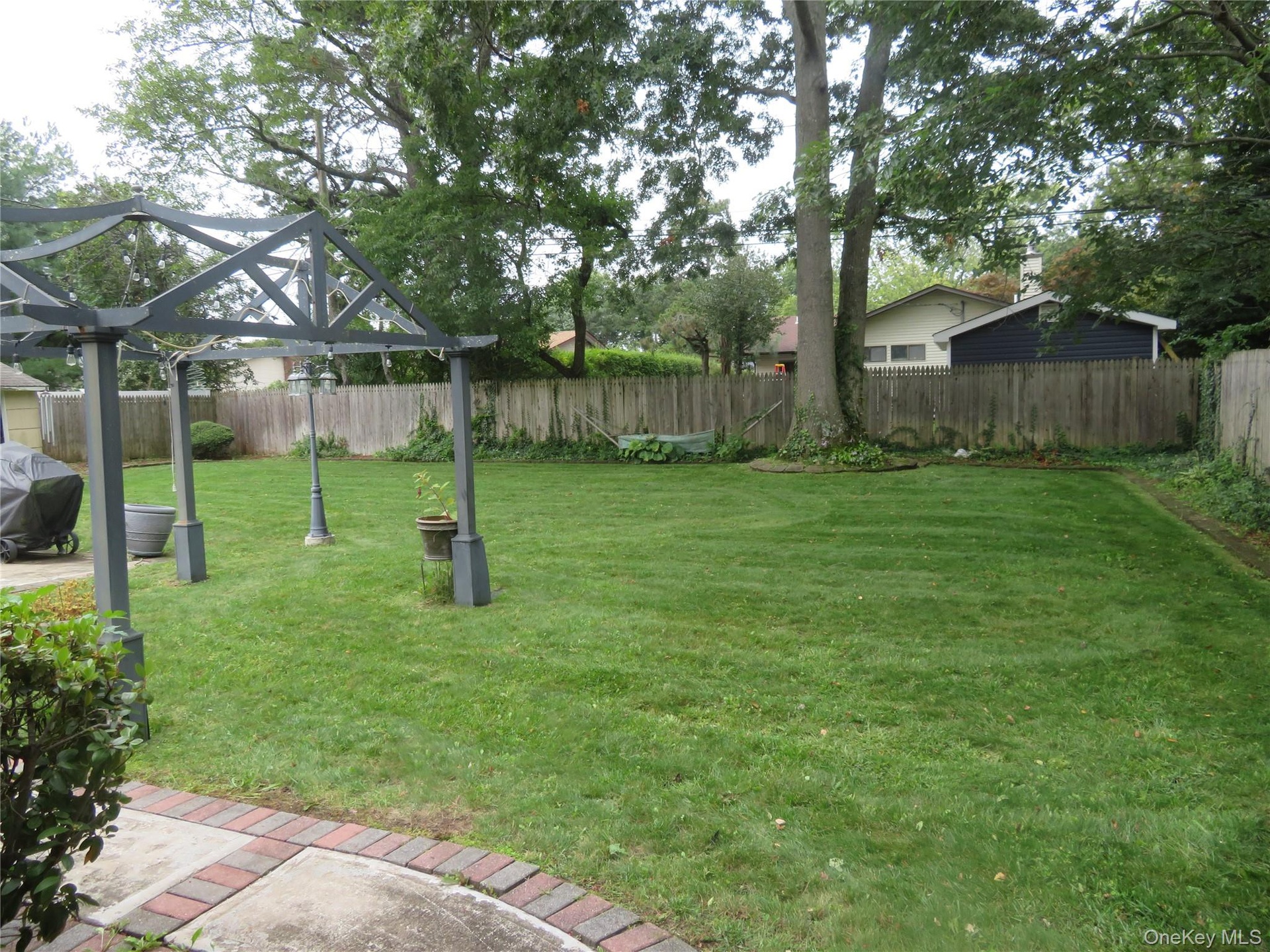 Expansive green lawn, mature trees, wood fence enclosure, and a decorative pergola structure