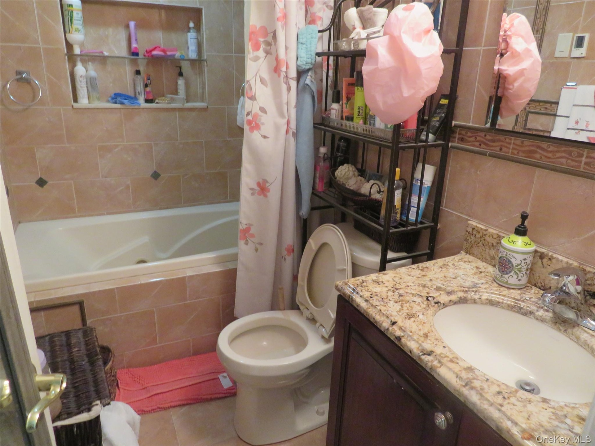 Brown tiled bathroom featuring a built-in bathtub, a vanity with a granite countertop, and a built-in shelf