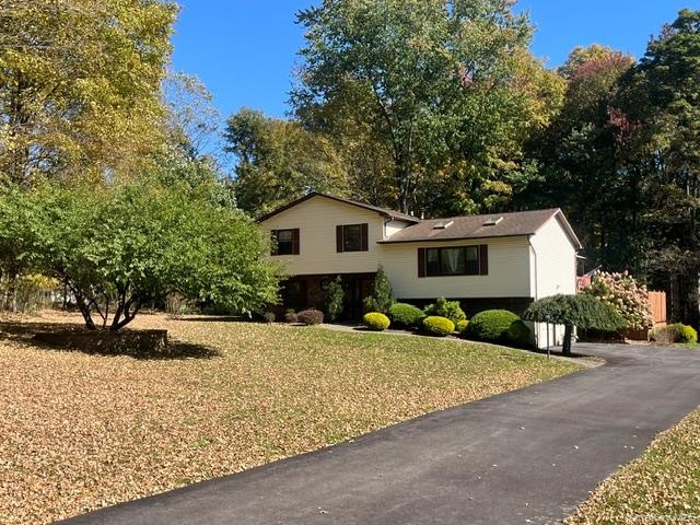 Siding exterior with dormer windows, surrounded by mature trees and landscaping, featuring a paved driveway and an expansive front lawn
