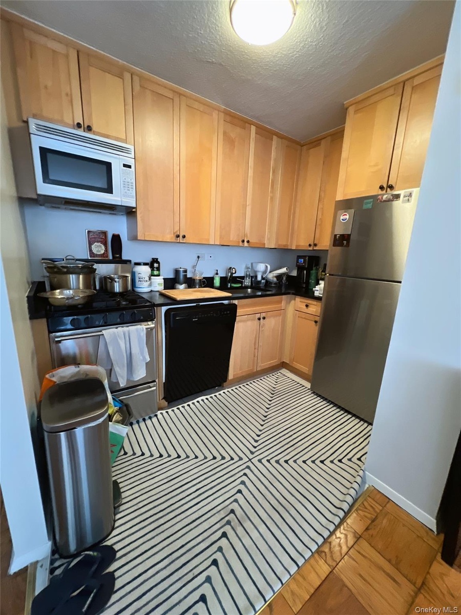 Kitchen featuring dark countertops, a textured ceiling, stainless steel appliances, and light brown cabinetry