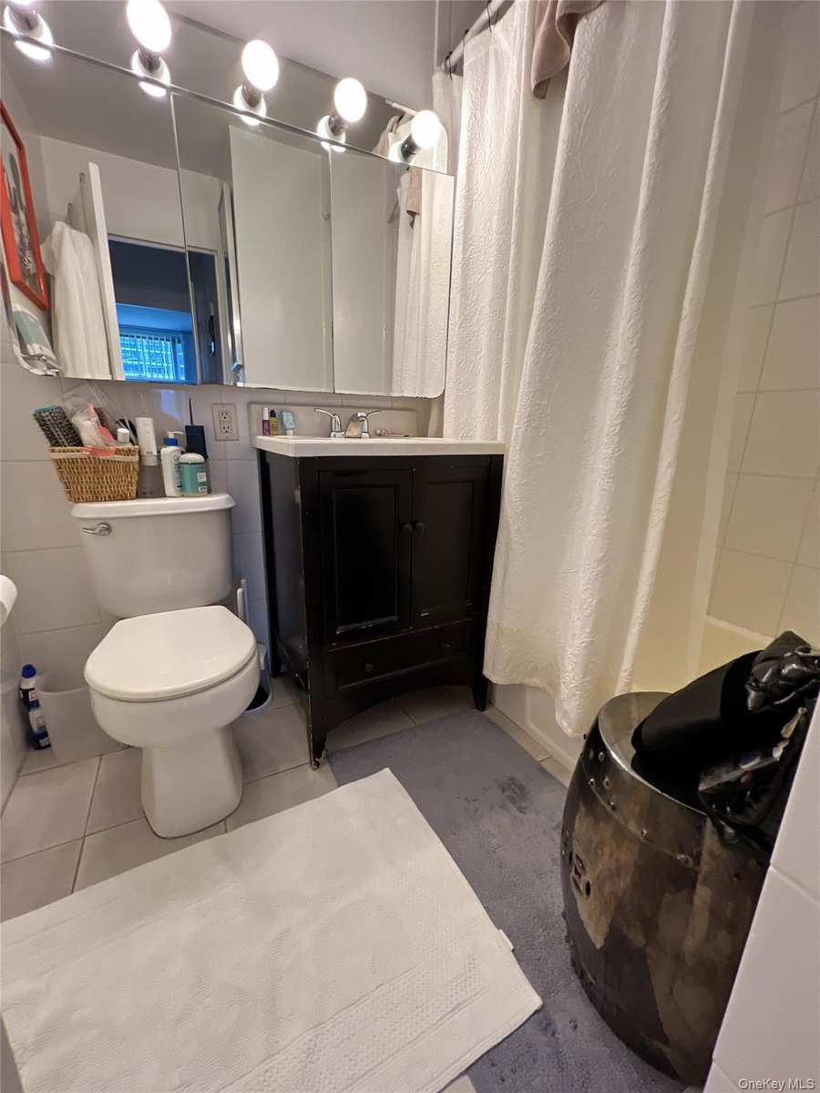Bathroom featuring tile patterned flooring, vanity, shower / bath combo, and tile walls