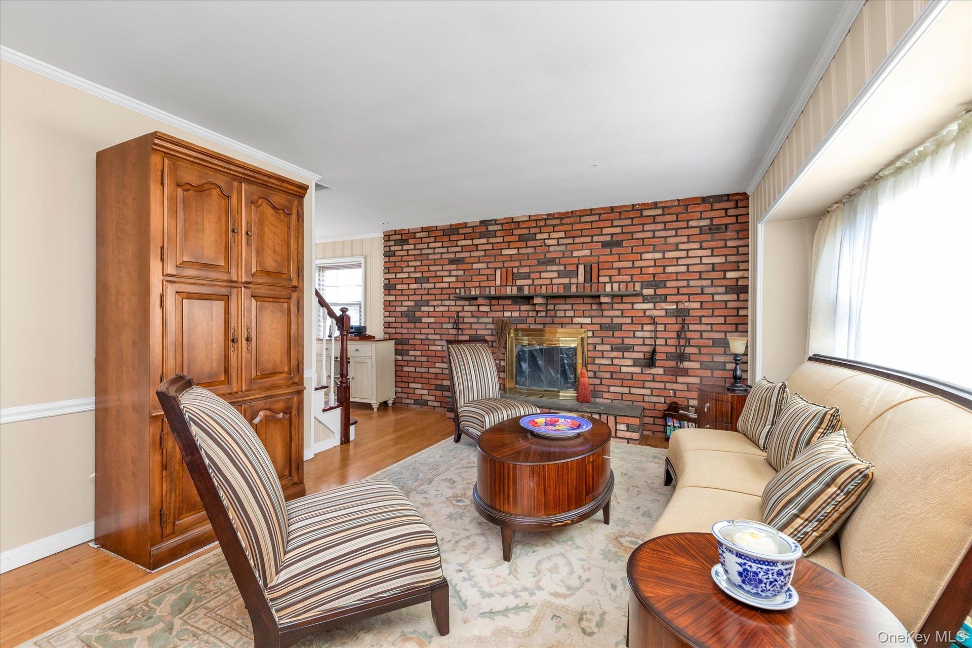 Brick fireplace with a stone hearth, hardwood flooring, and a large window