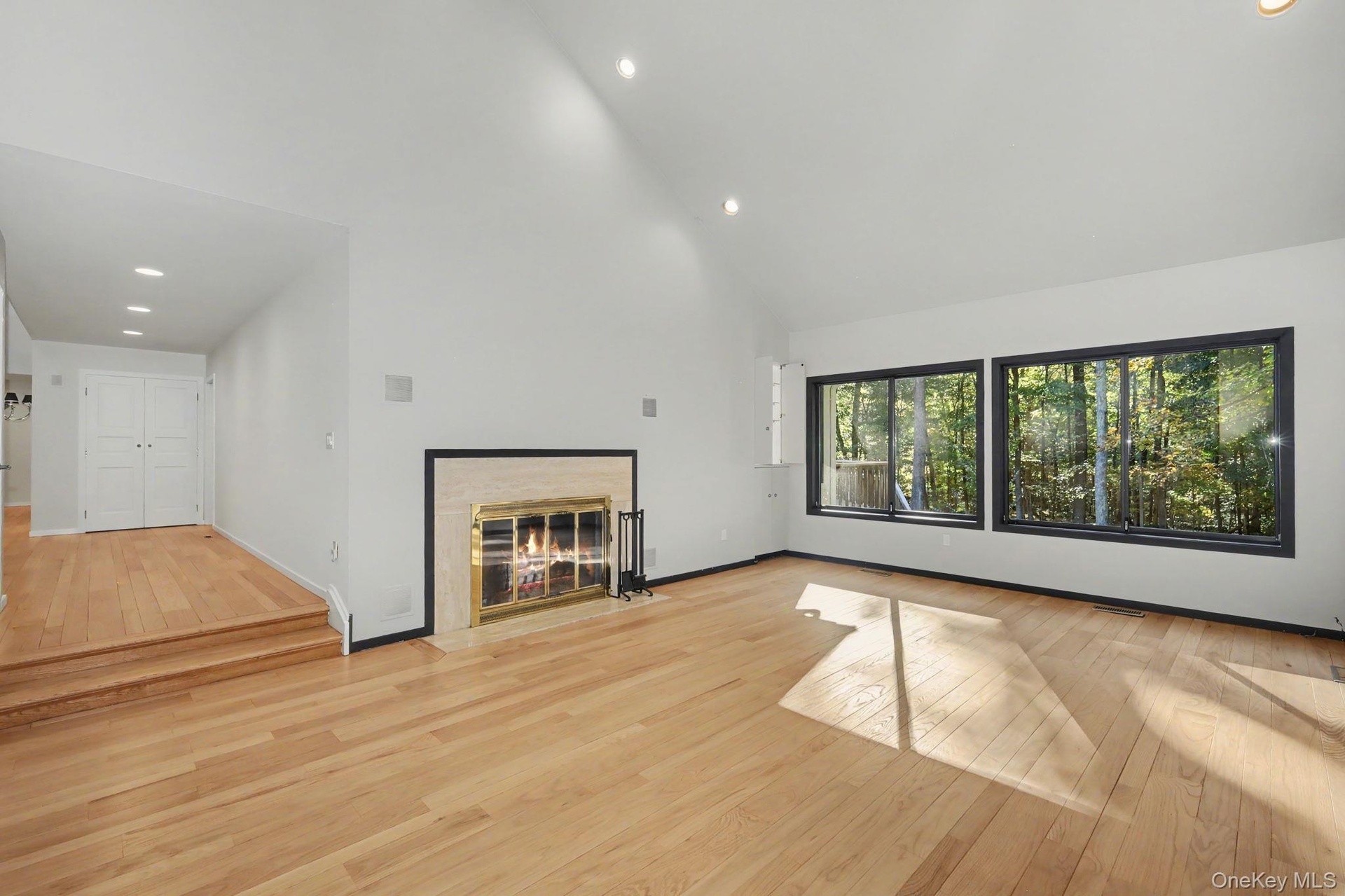 Generous living room with cathedral ceilings, fireplace, and expansive windows overlooking the wooded grounds.