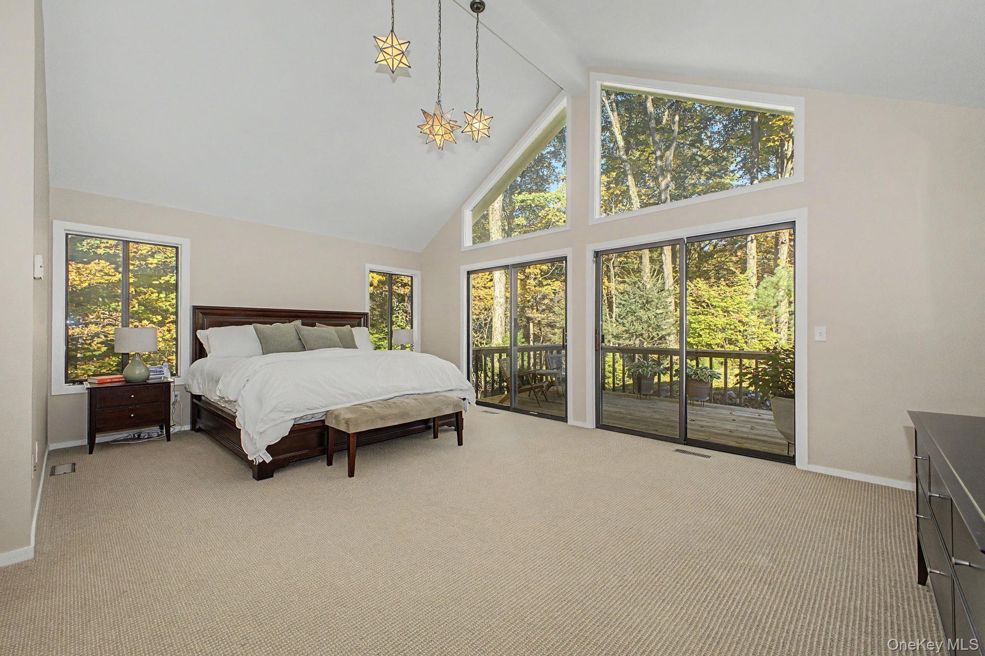 Primary bedroom retreat with soaring cathedral ceilings, expansive windows, and sliding doors to a private deck overlooking the wooded grounds.