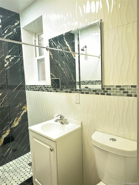 Shower with black and gold-veined tile, mosaic accent border, white wave-patterned wall tile, and a white vanity with an integrated sink