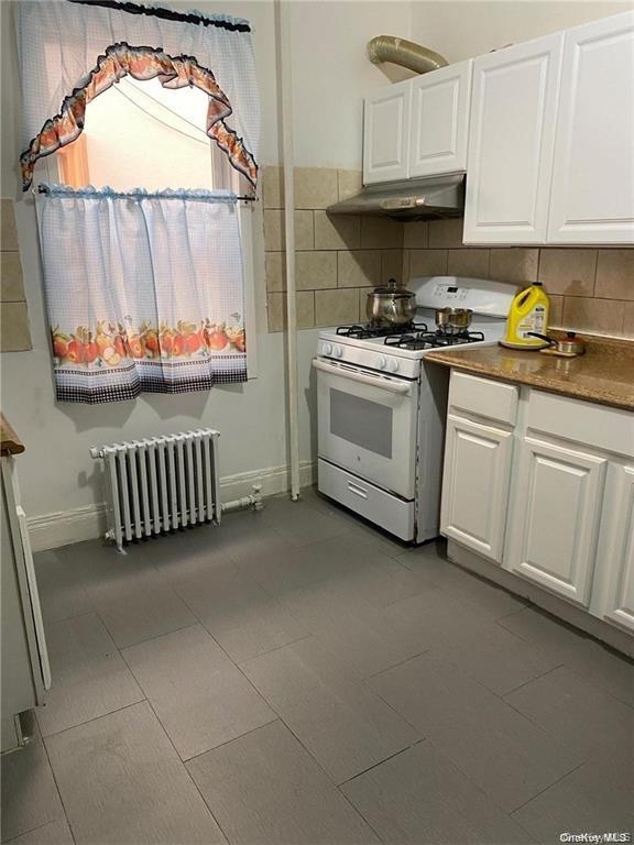 White cabinetry, gas range, metal range hood, stone-finish countertops, and tile flooring