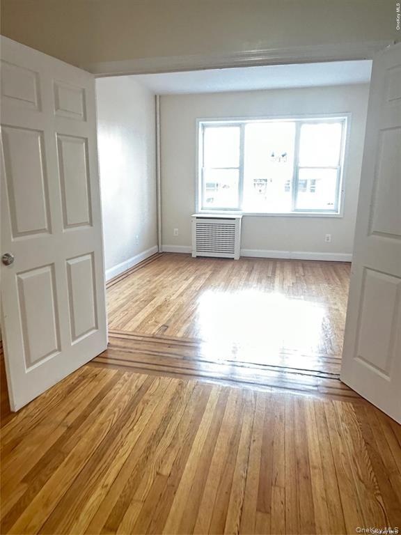 Hardwood flooring extending through an open doorway, white interior doors, and a window with a radiator below