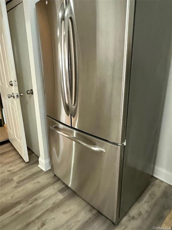 Stainless steel French door refrigerator with a bottom freezer drawer, complemented by wood-finish flooring