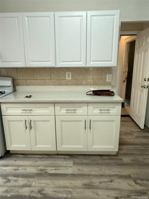 White upper and lower cabinetry, light-toned countertop, tile backsplash, and wood-finish flooring