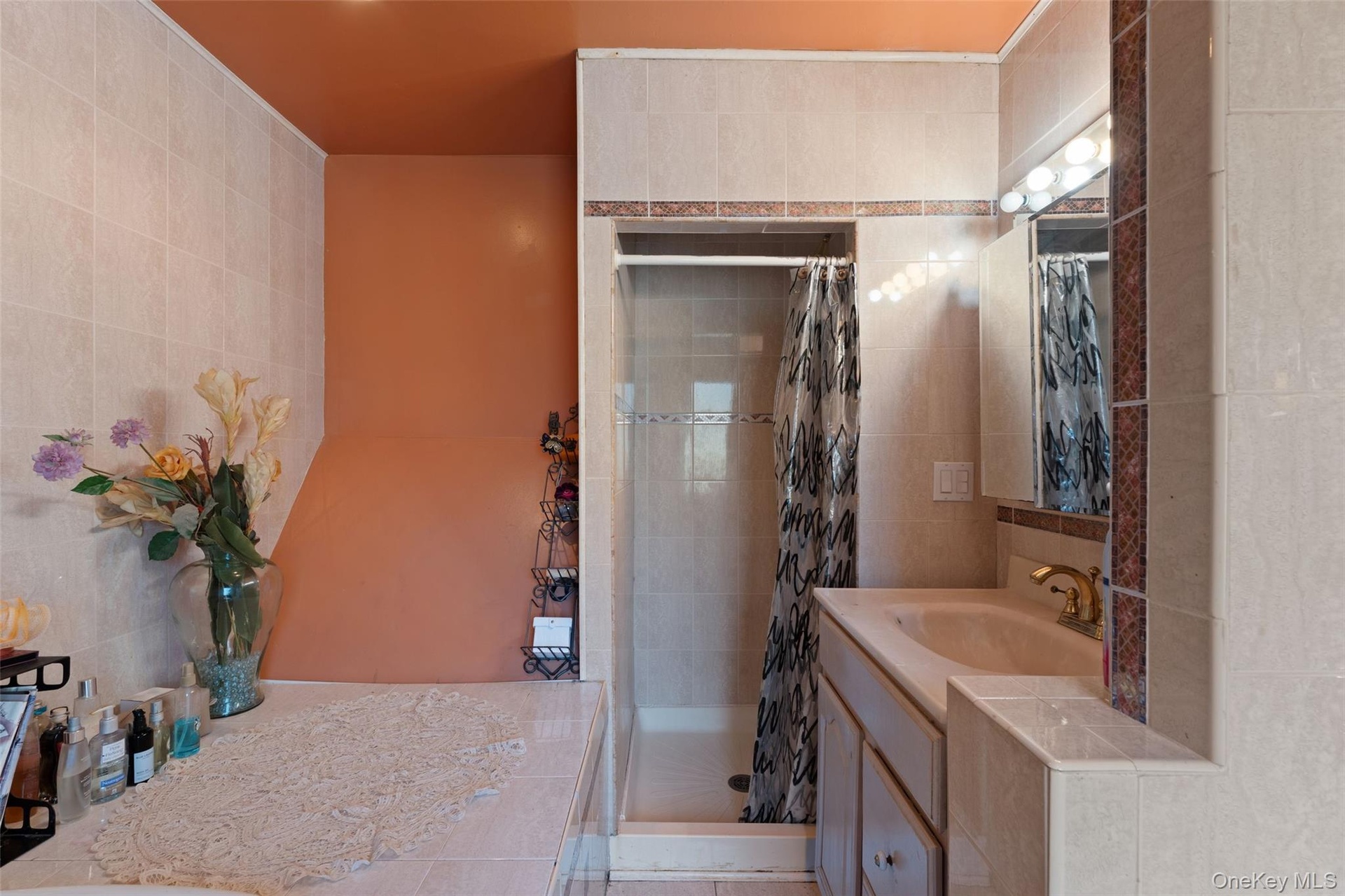 Tiled bathroom featuring a jacuzzi, built-in shower, vanity with sink, and wall-mounted lighting.