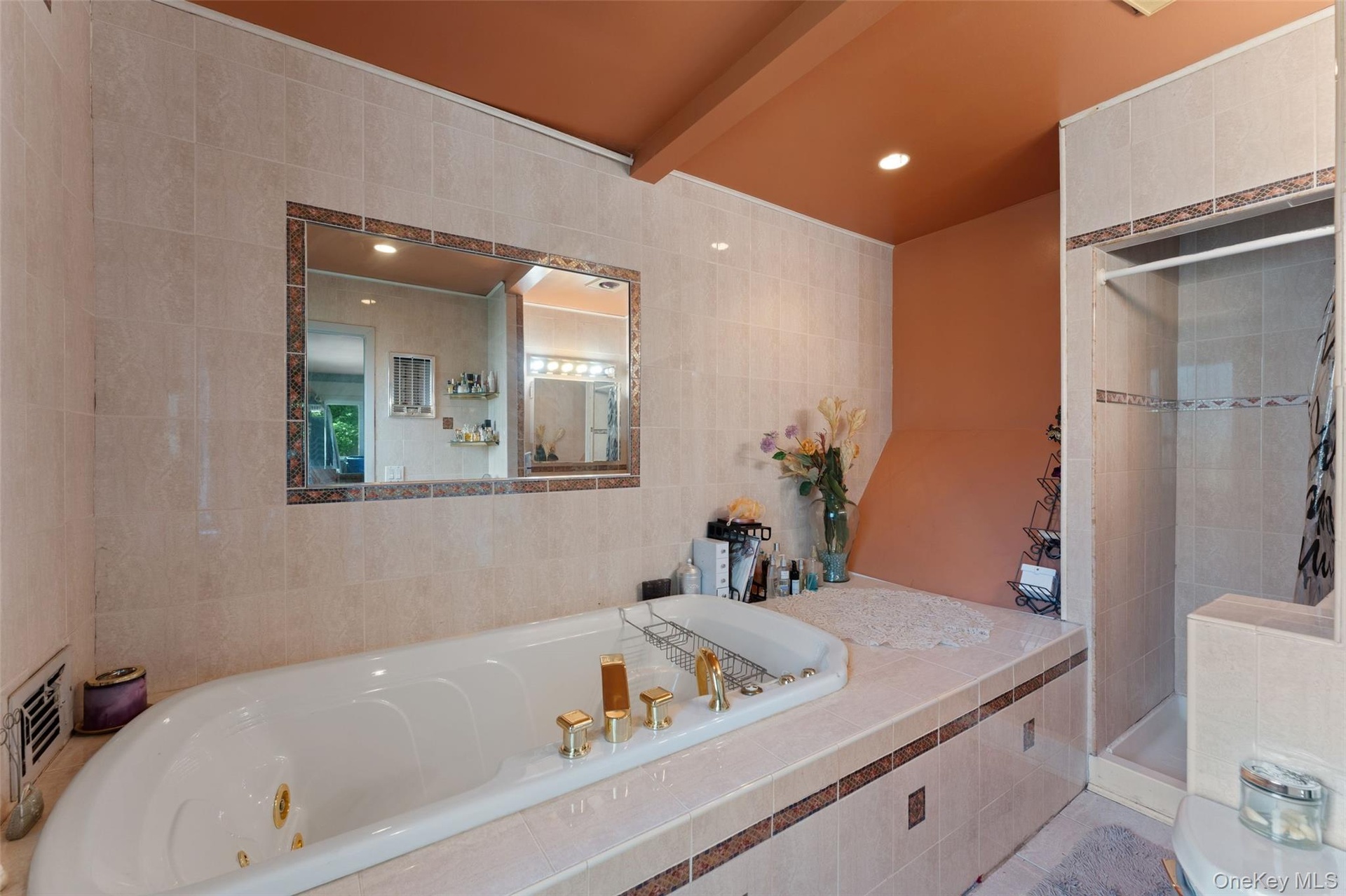 Tiled bathroom featuring a jacuzzi, built-in shower, vanity with  sink, and wall-mounted lighting.