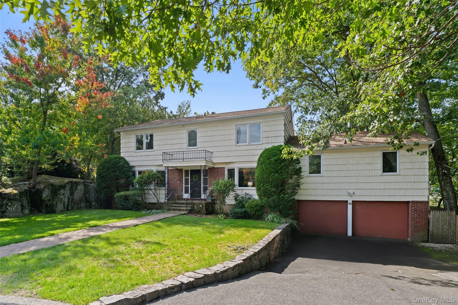 Welcome to 16 Cadillac Drive. Two-story residence with a brick paver walkway, mature trees, and a front lawn.