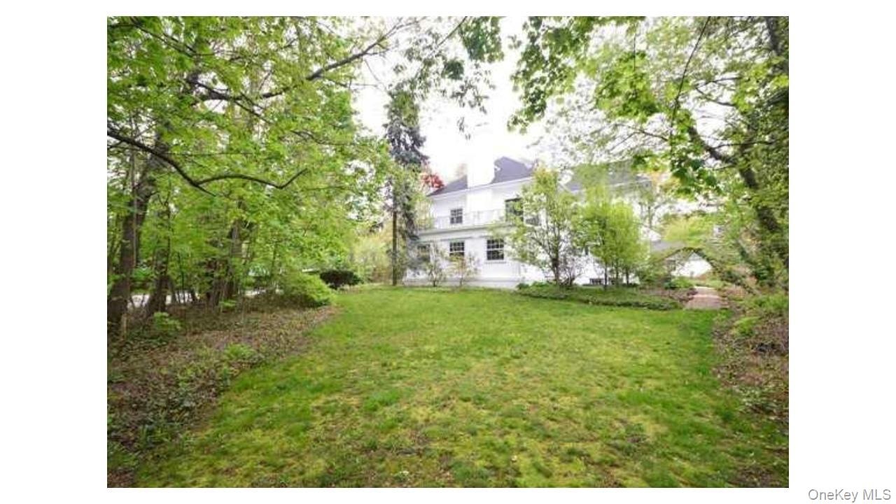Expansive lawn surrounded by mature trees, featuring a white multi-story residence with multiple windows and a balcony