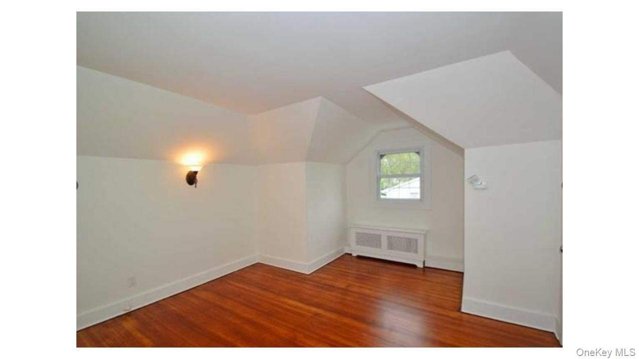 Hardwood flooring, painted white trim, window, wall-mounted sconce, and radiator cover