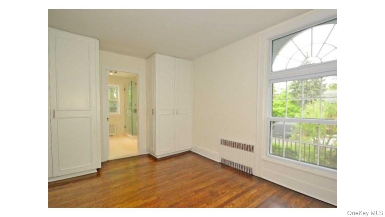 Wood-finish flooring with built-in cabinetry, an arched window, and an en-suite bathroom with a glass-enclosed shower