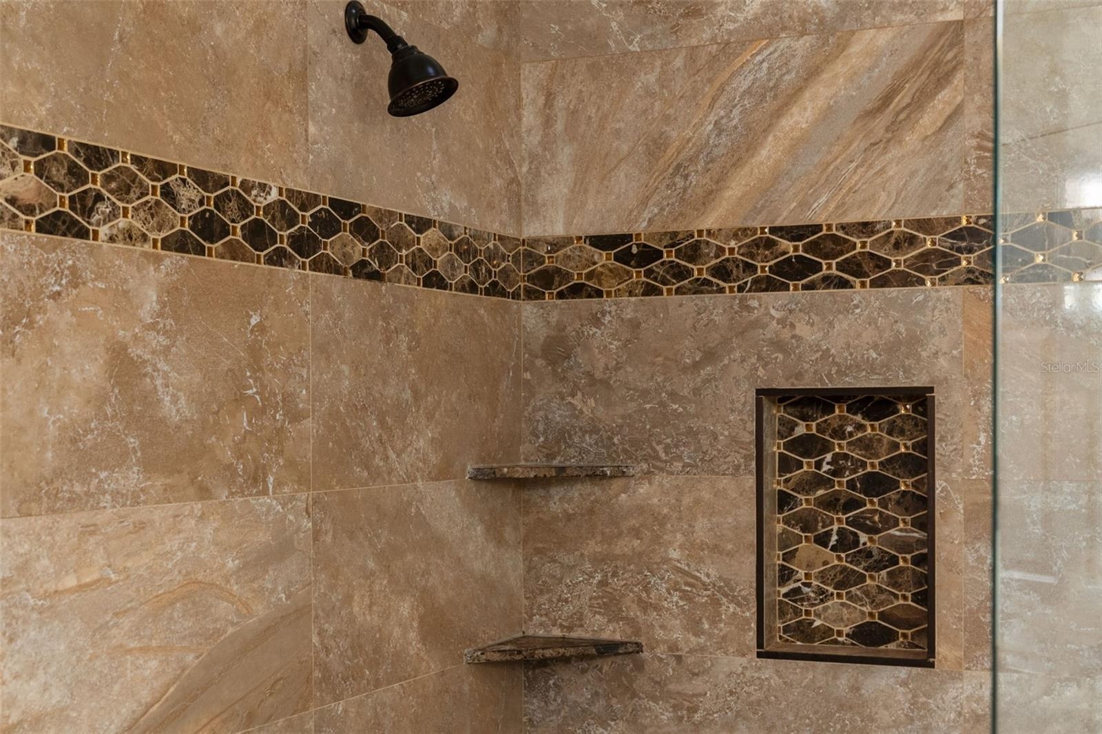 A generous shower with mosaic detailing, built-in shelves, and a recessed niche for everyday essentials.