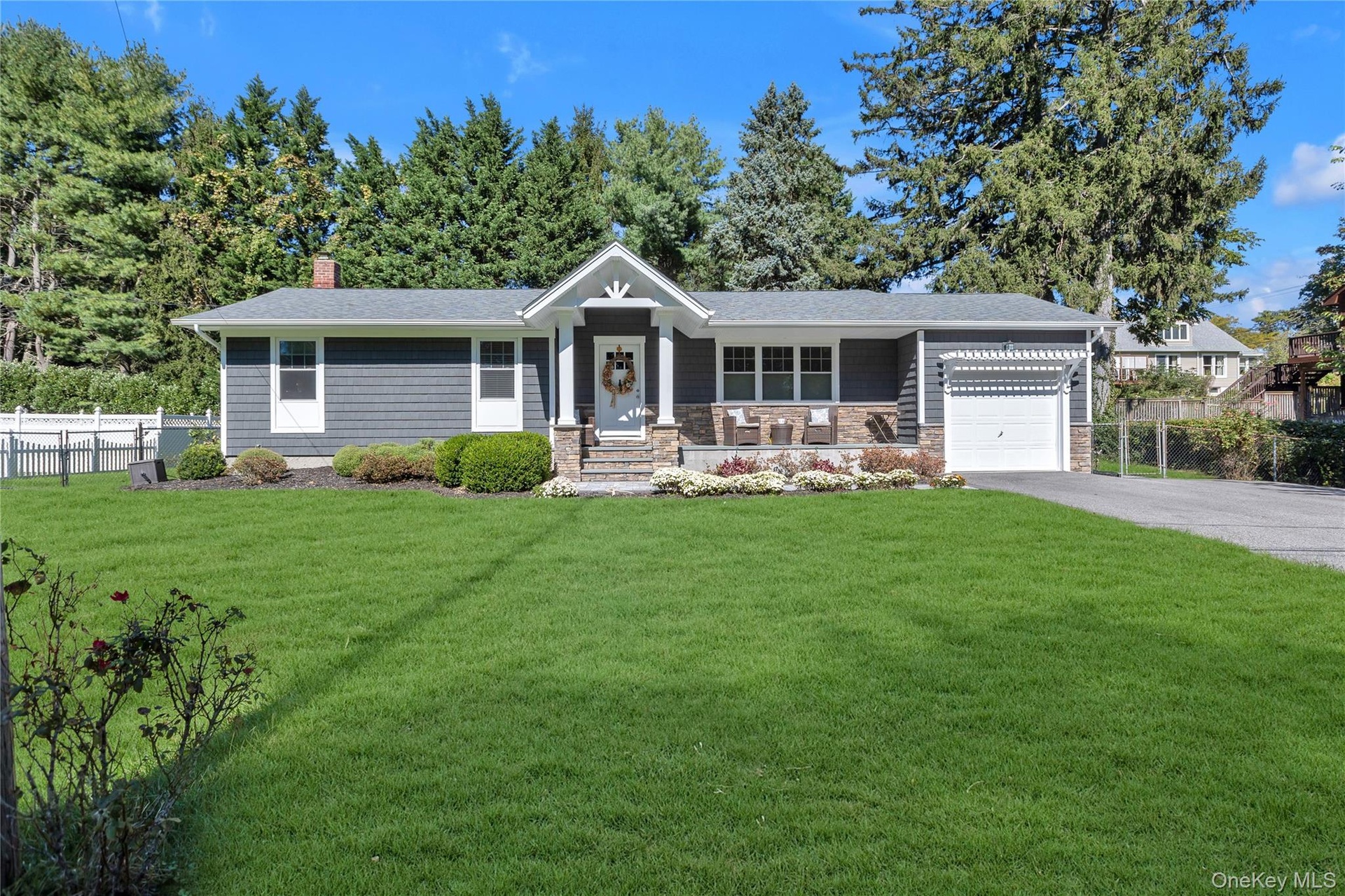 Shingle siding exterior with stone accents, a covered front porch, an attached garage, a paved driveway, and a front lawn