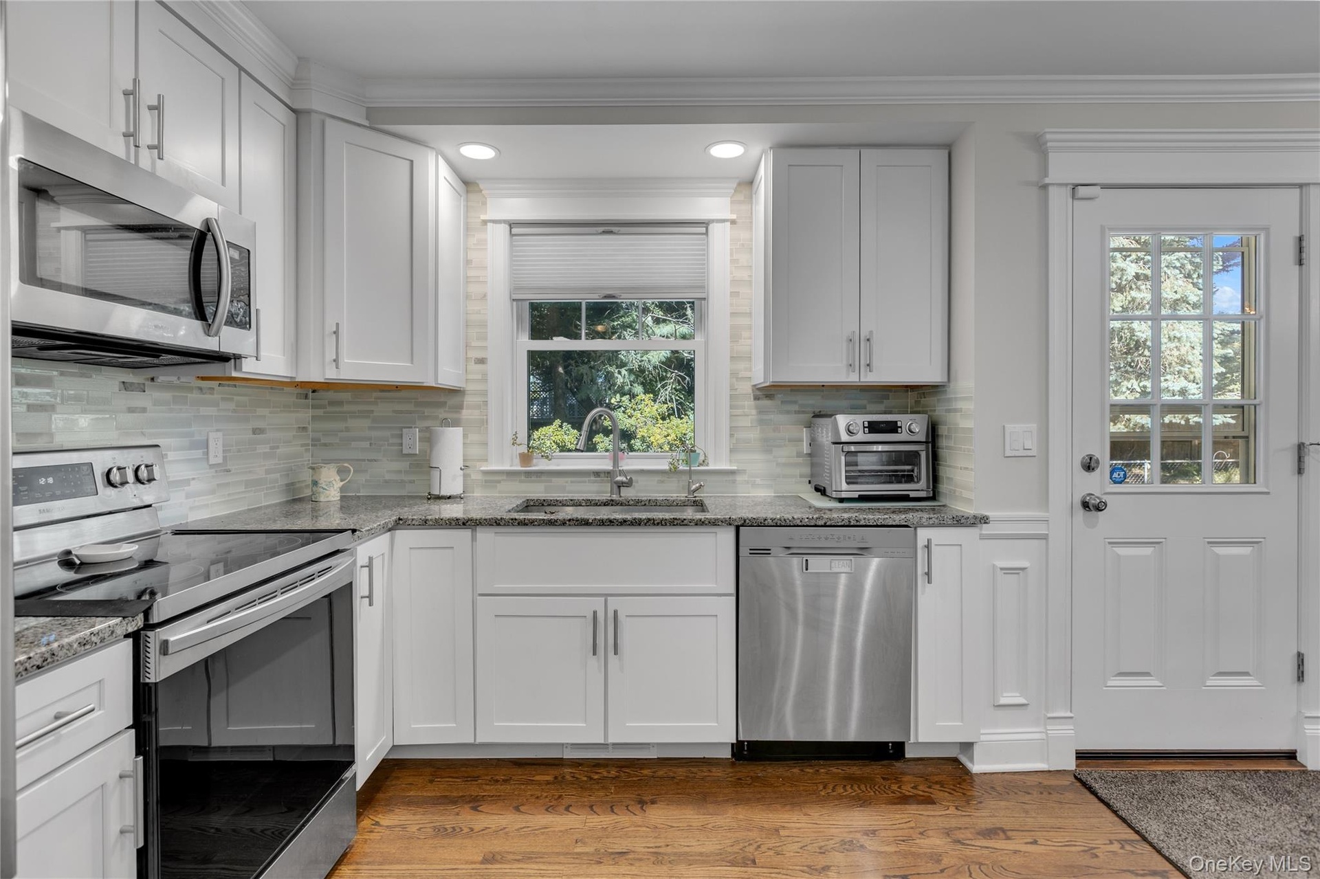 Kitchen featuring white cabinetry, stainless steel appliances, granite countertops, a tiled backsplash, and wood-finish flooring, access to backyard r