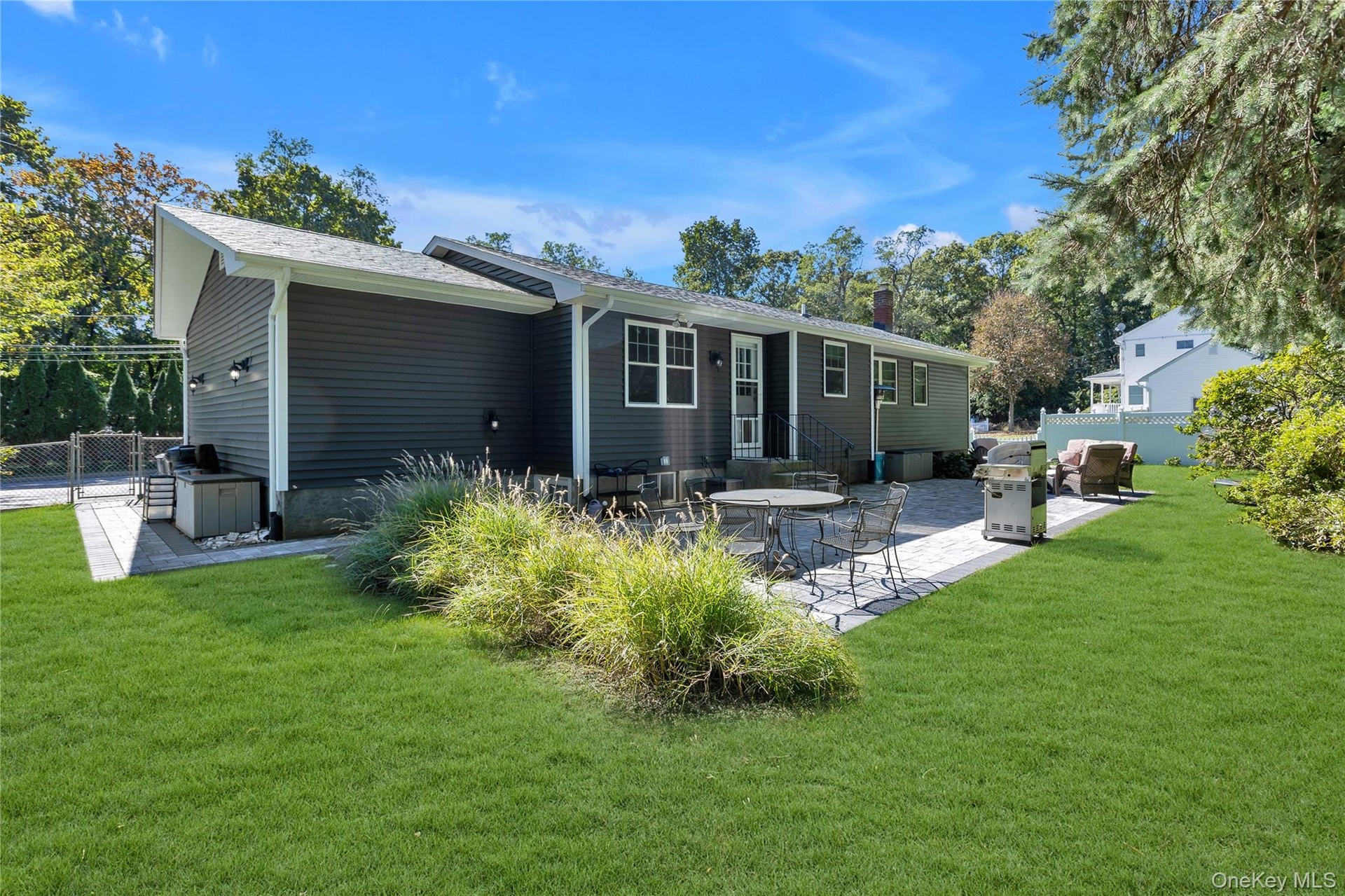 Expansive backyard featuring a manicured lawn, paver patio, mature trees, and dark gray siding