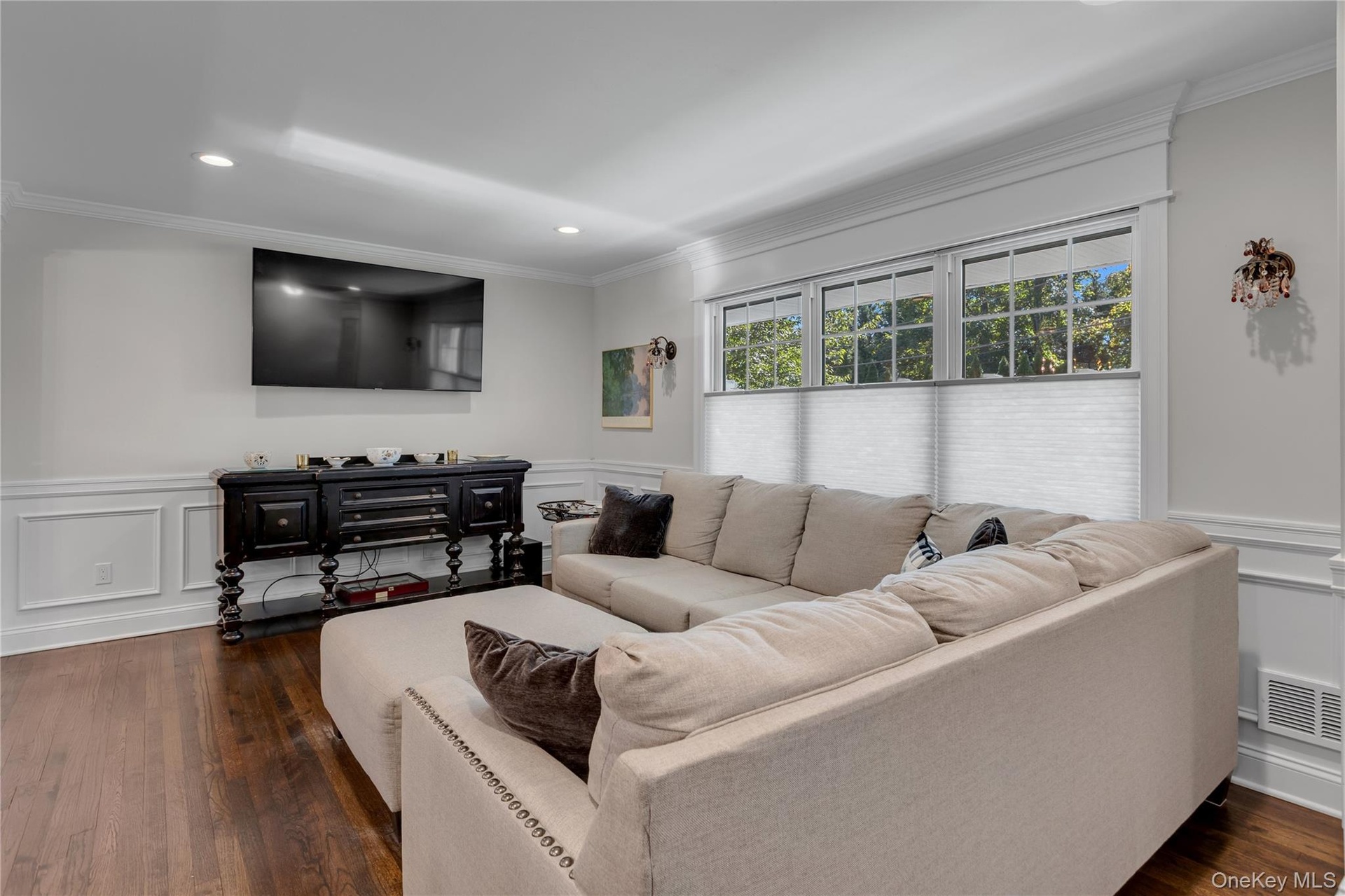 Hardwood flooring with a satin finish, white wall paneling, recessed lighting, and crown molding