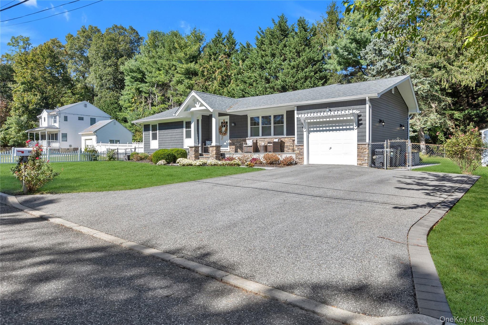 Ranch-style exterior with gray horizontal siding and stone accents. Double wide driveway with access to one car attached garage,